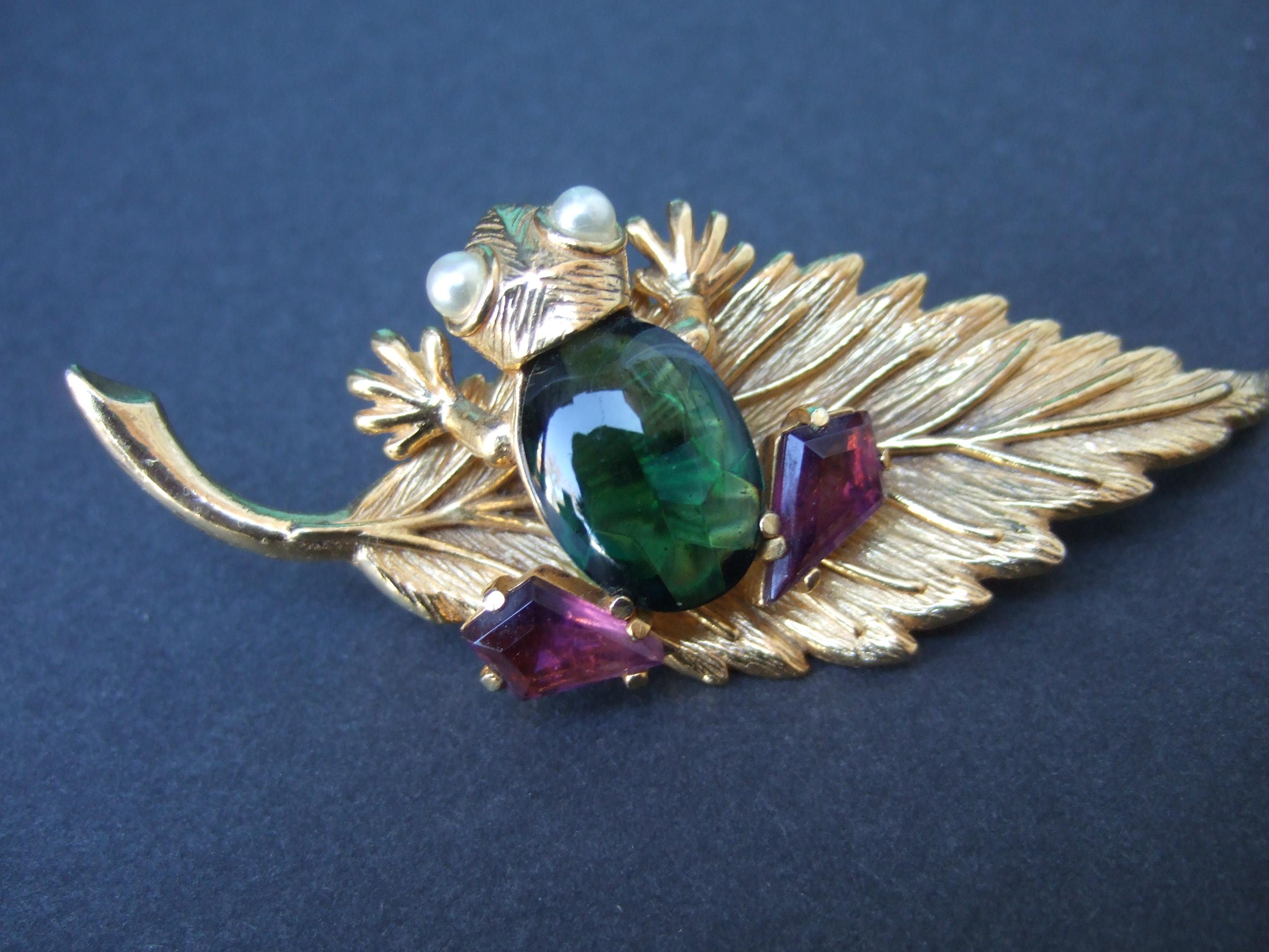 SCHIAPARELLI Seltene charmante Froschbrosche mit Juwelen um 1960
Die einzigartige Brosche ist mit einem bezaubernden Frosch gestaltet, der auf einer 
auf einem vergoldeten Lilienblatt aus Metall

Der Frosch ist mit einem glatten grünen Glascabochon