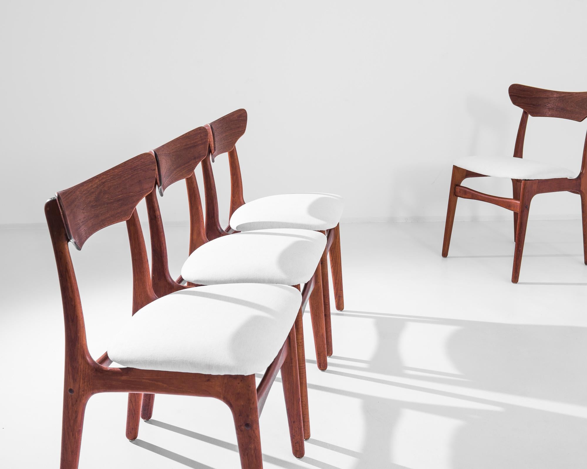 A set of four midcentury Modernist wooden dining chairs by Danish furniture designers Schionning & Elgaard. This design embodies the characteristic silhouette for which these designers are known — the rounded backrest, the eager forward slant of the