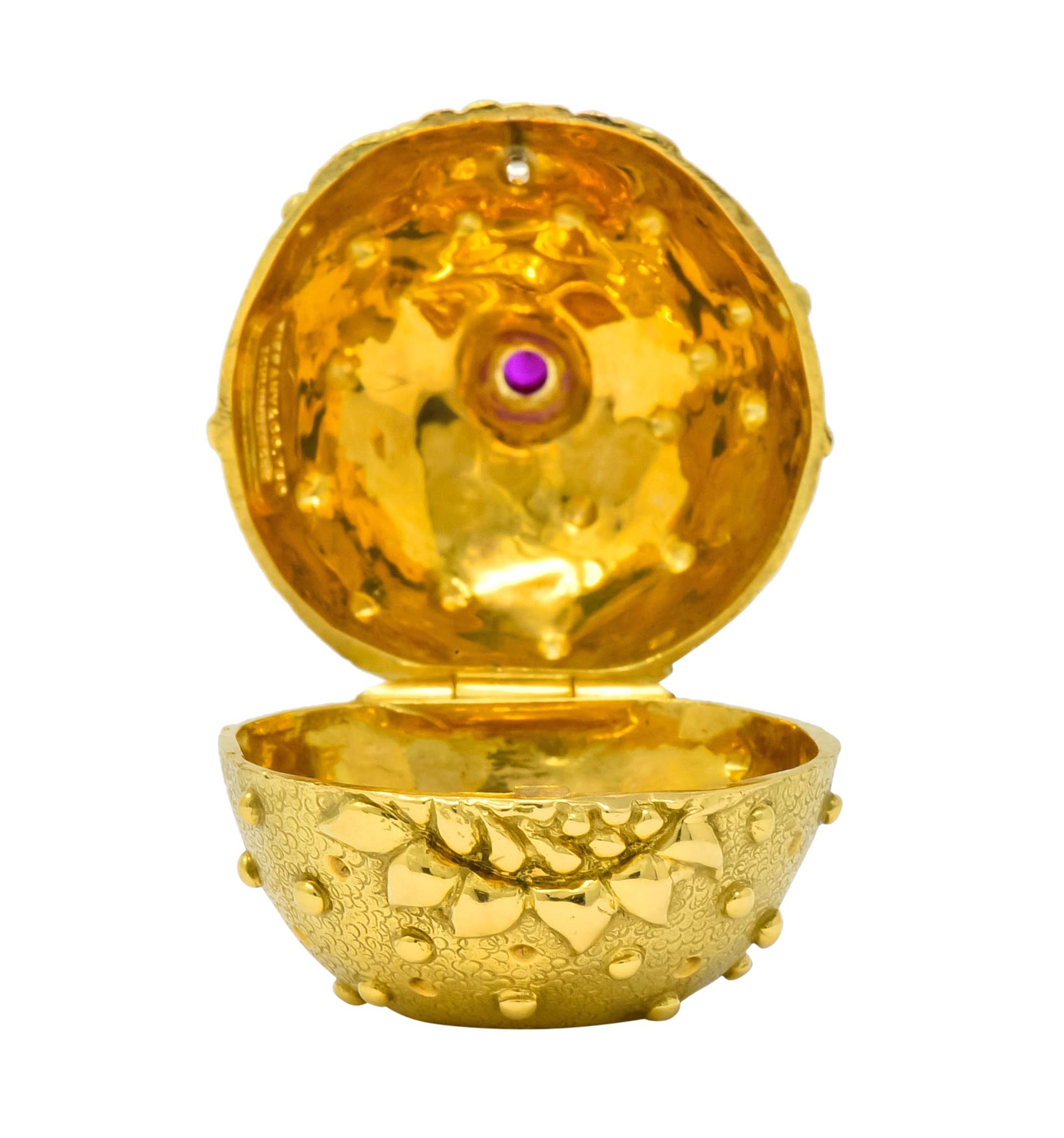 Designed as pomegranate shaped repousse pill box, stippled matte gold decorated throughout by gold bead detail

Featuring front facing foliate motif and topped by foliate stem erupting into a bezel set rose cut ruby weighing approximately 0.20