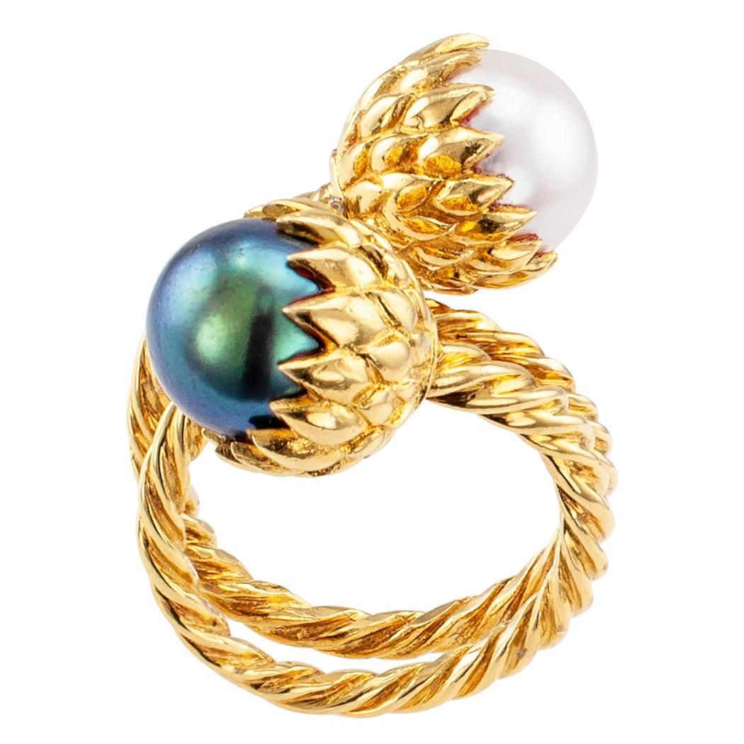 Tiffany & Co Schlumberger black and white pearl gold ring circa 1970. The design features a pair of pearls measuring approximately 9 mm, one black and one white, both set vertical to the fingernail on an 18-karat yellow gold cable mounting that