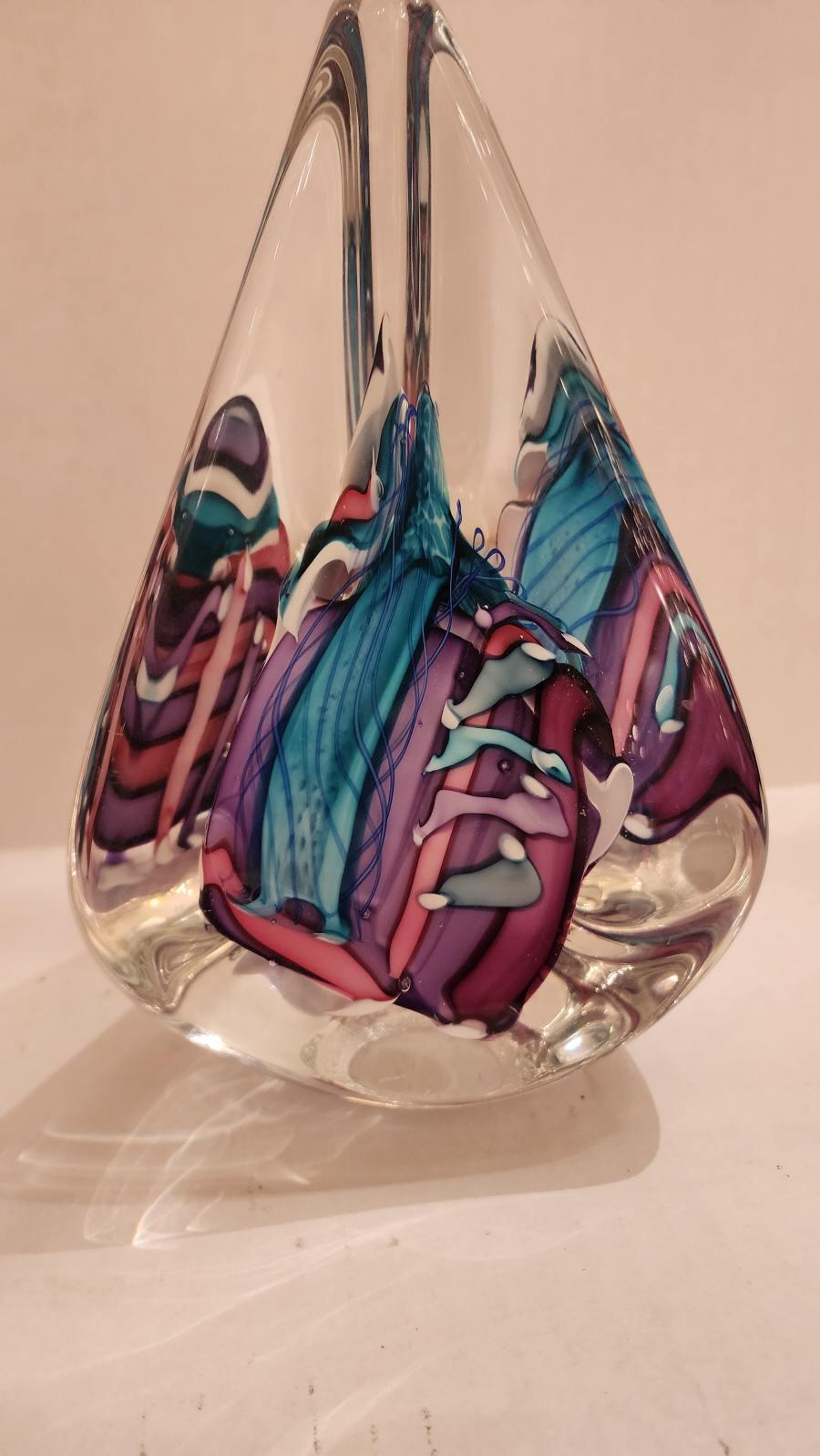 Questa inserzione presenta una scultura astratta in vetro a forma di goccia con pezzi di vetro astratti viola, rosa e blu incastonati. Questo pezzo è stato creato dagli artisti Michael Schmidt e Sonia Rhea. 

Gli artisti si sono conosciuti a