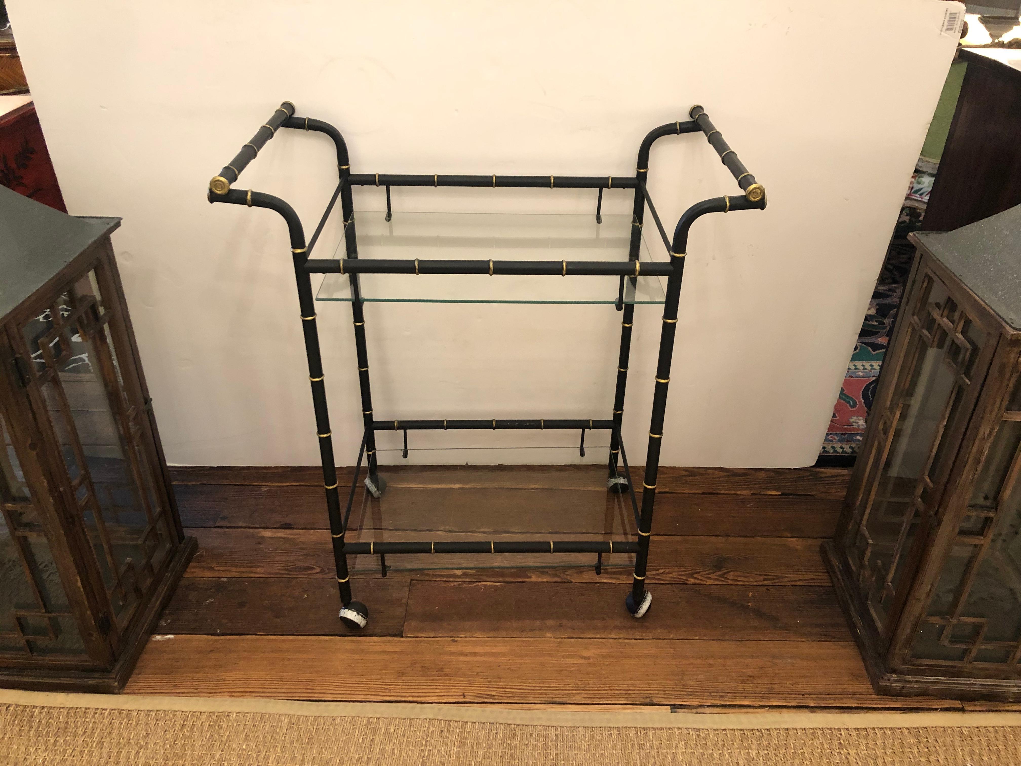Hollywood Regency metal two tier bar cart having black and gold faux bamboo handles and frame and two glass shelves on casters. Rolls smoothly and is a versatile functional bar cart, and great as an end table too.
Measures: 28 H to top shelf
5.75