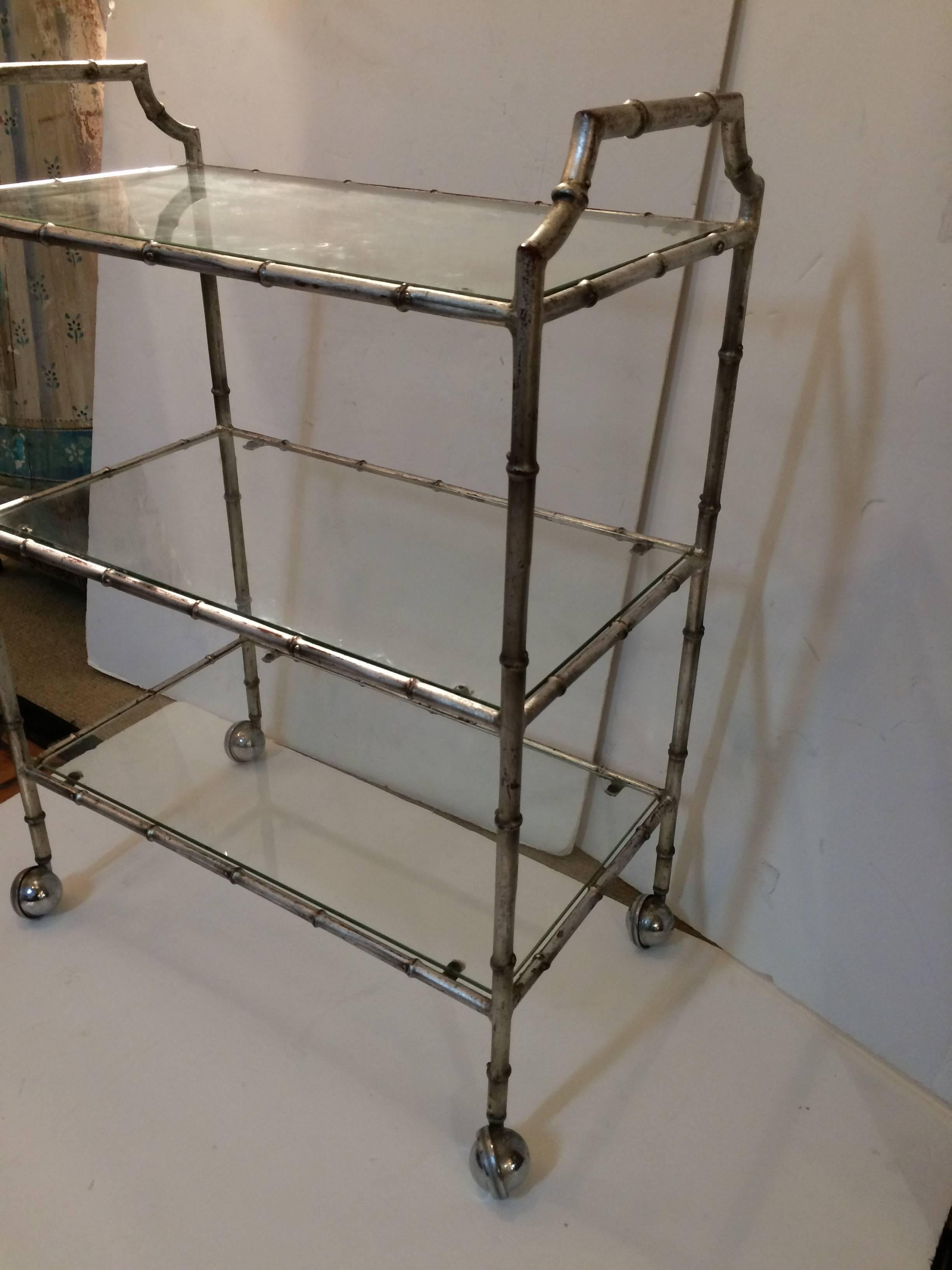 Very stylish iron faux bamboo bar cart having silver leaf coloration with reddish undercoat, offering an out of the ordinary three tiers and chrome ball casters for easy rolling.
 
