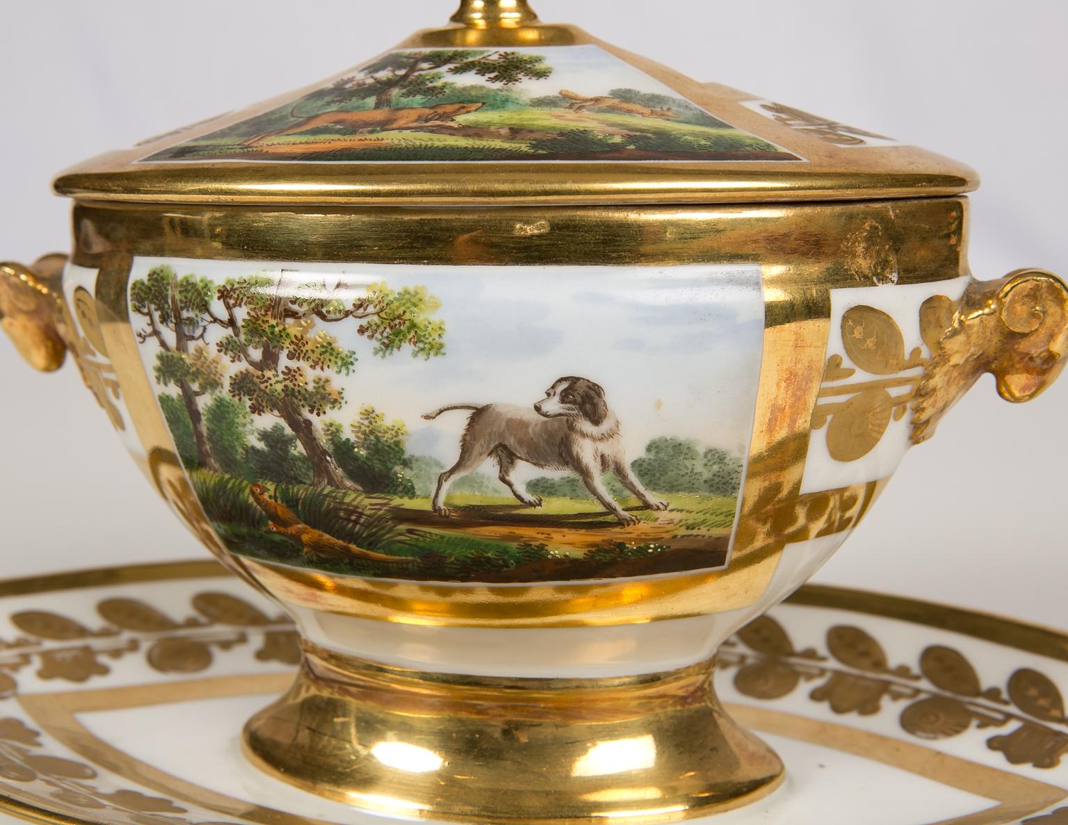 A Schoelcher porcelain small tureen showing hunting dogs in a French country landscape. The tureen and cover have hand-painted panels showing romanticized scenes of country life.
The panels feature figural or hunting scenes: one showing a dog