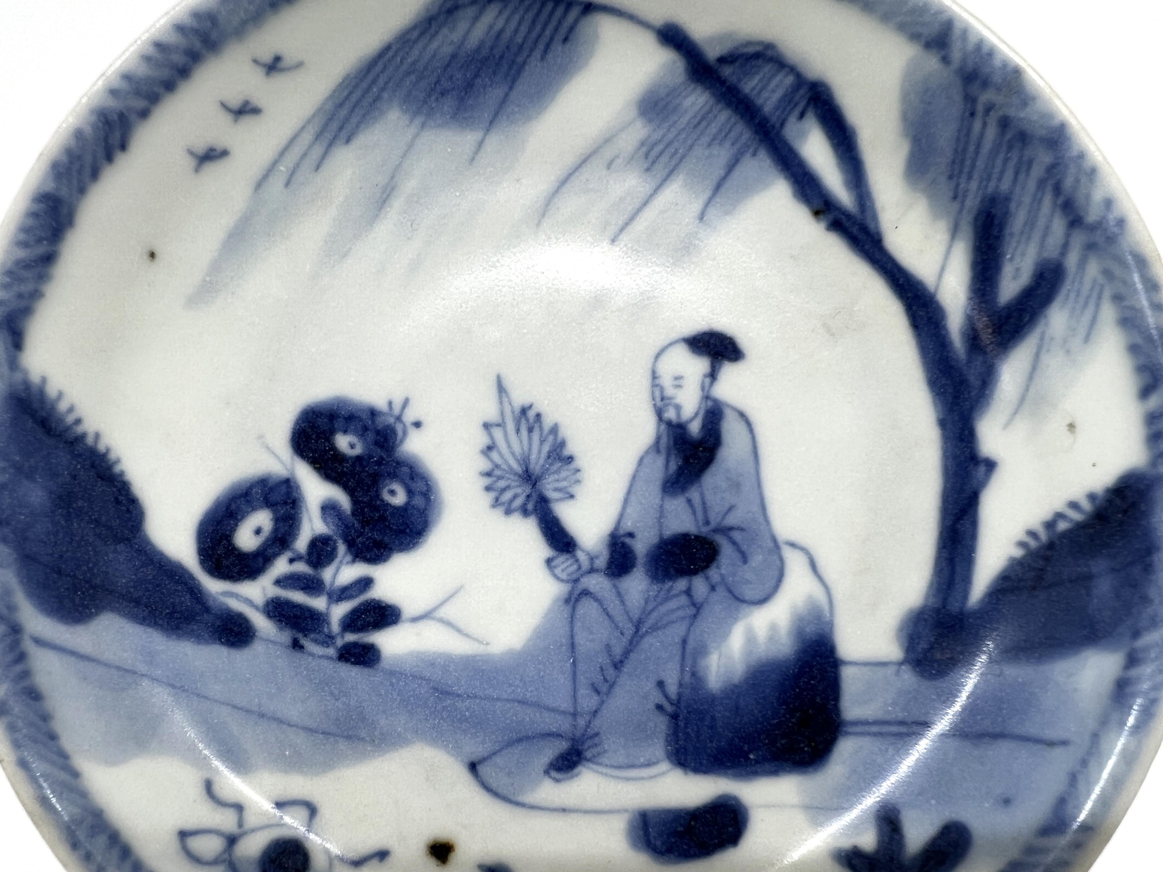 The central motif features a figure, likely a scholar, seated in a tranquil outdoor setting. This person is holding what seems to be a fan, a common accessory for scholars in traditional Chinese depictions, suggesting a moment of leisure or