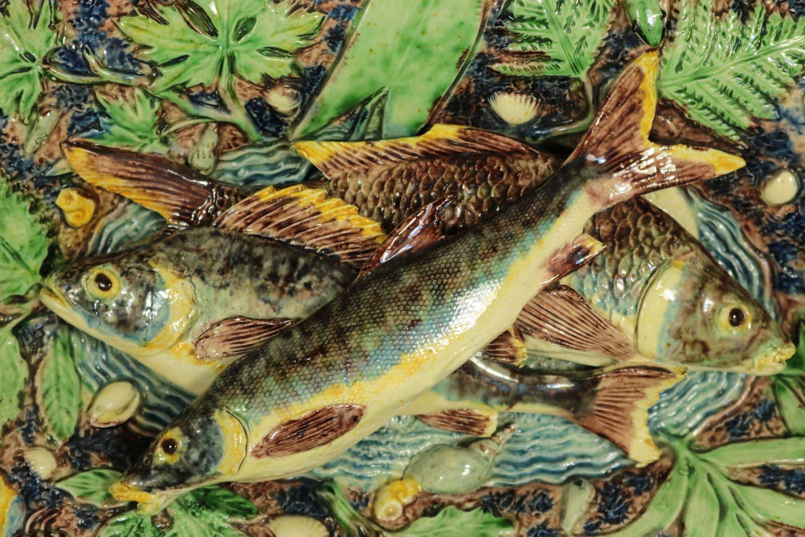 Wandteller aus französischer Palissy-Majolika der Pariser Schule mit drei sich überlappenden Fischen auf einem Grund mit Wassereffekt in der Mitte. Eine Eidechse, Schalentiere, Insekten und Blätter am Rand. Färbung: grün, blau, braun, sind