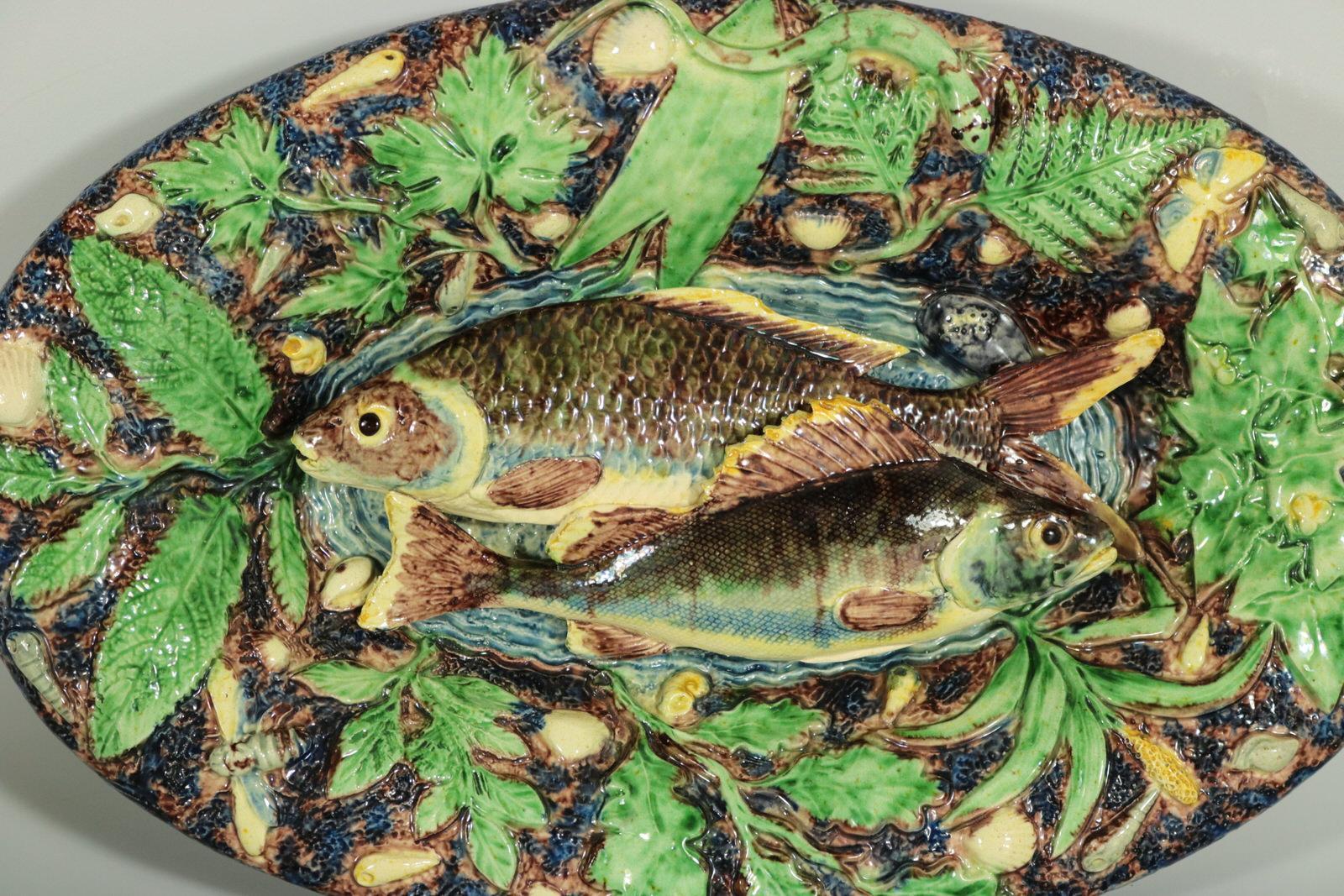 School of Paris French Palissy Majolica wall platter which features two overlapping fish on a water-effect ground, to the centre. A lizard, shellfish, insects and leaves around the rim. Coloration: Green, blue, brown, are predominant. Attribution,