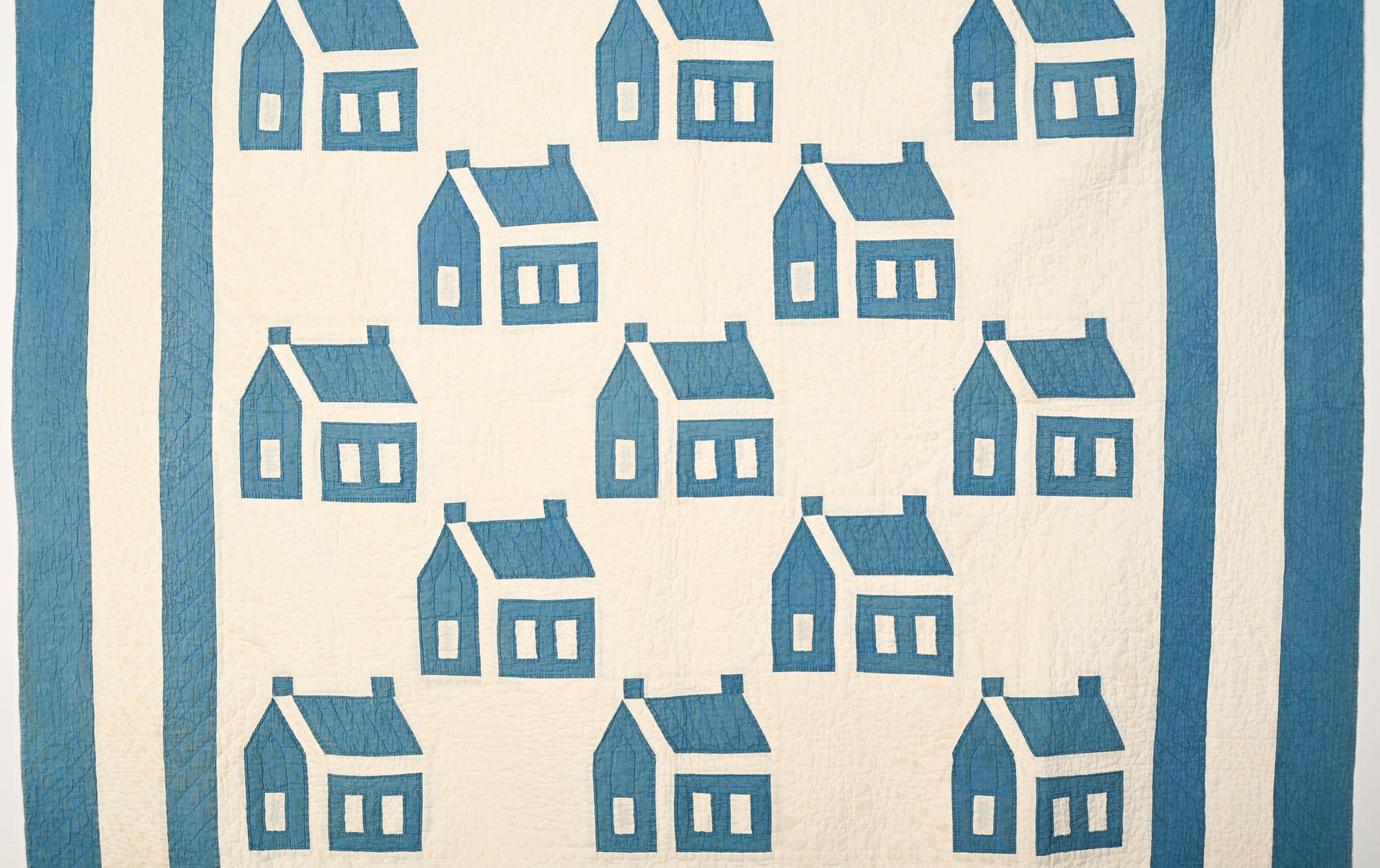Quilt classique à motifs d'école dans une belle nuance de bleu.  Les bâtiments sont joliment agencés. Les triples frontières permettent de contenir les maisons. Joliment matelassé dans une variété de motifs incluant des câbles ;  lignes diagonales