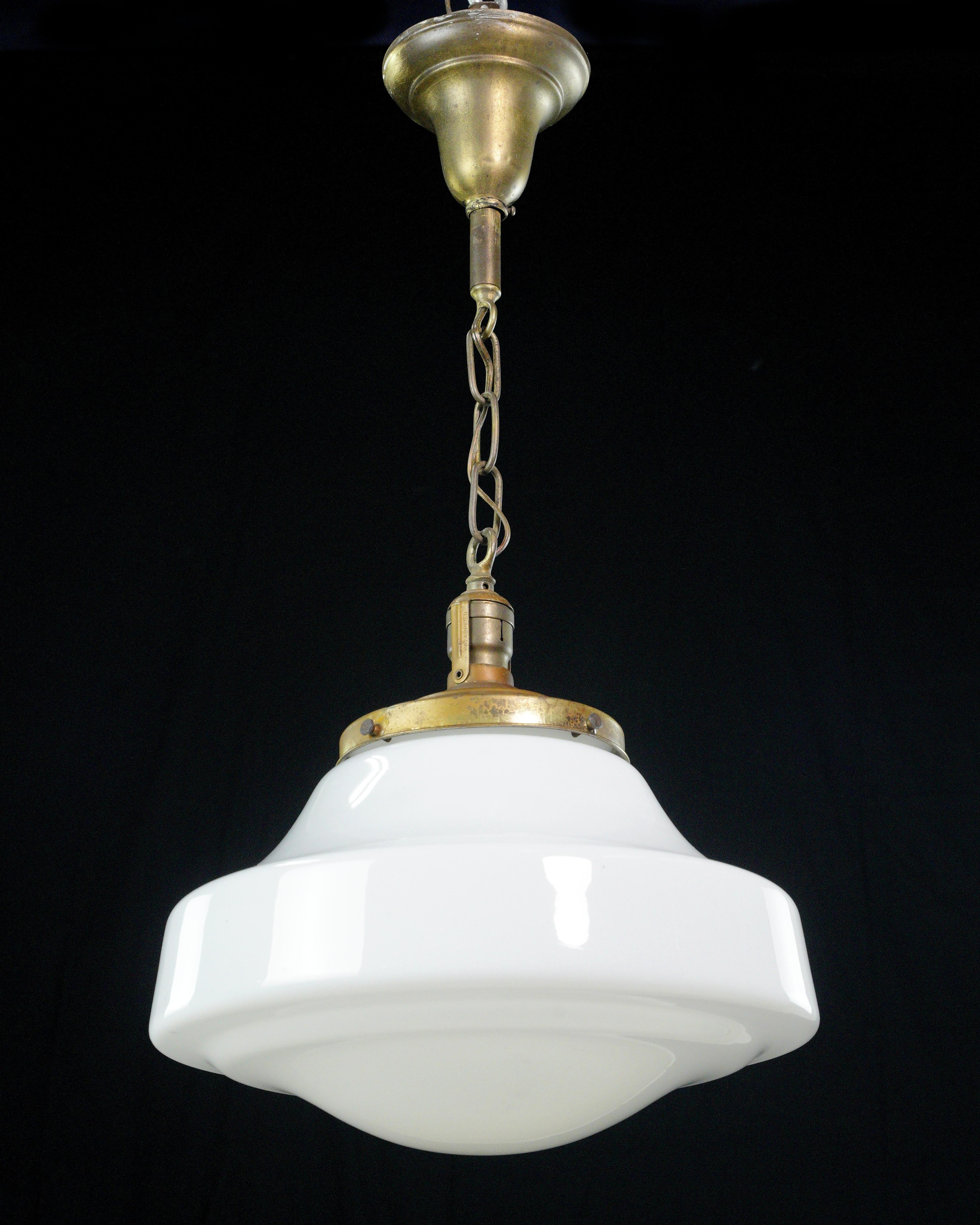 Cette lampe suspendue antique est un superbe luminaire doté d'un globe en verre au lait blanc inspiré des écoles et d'une élégante chaîne en acier au fini laiton. Il allie une beauté intemporelle à une touche de sophistication. Il est équipé d'une