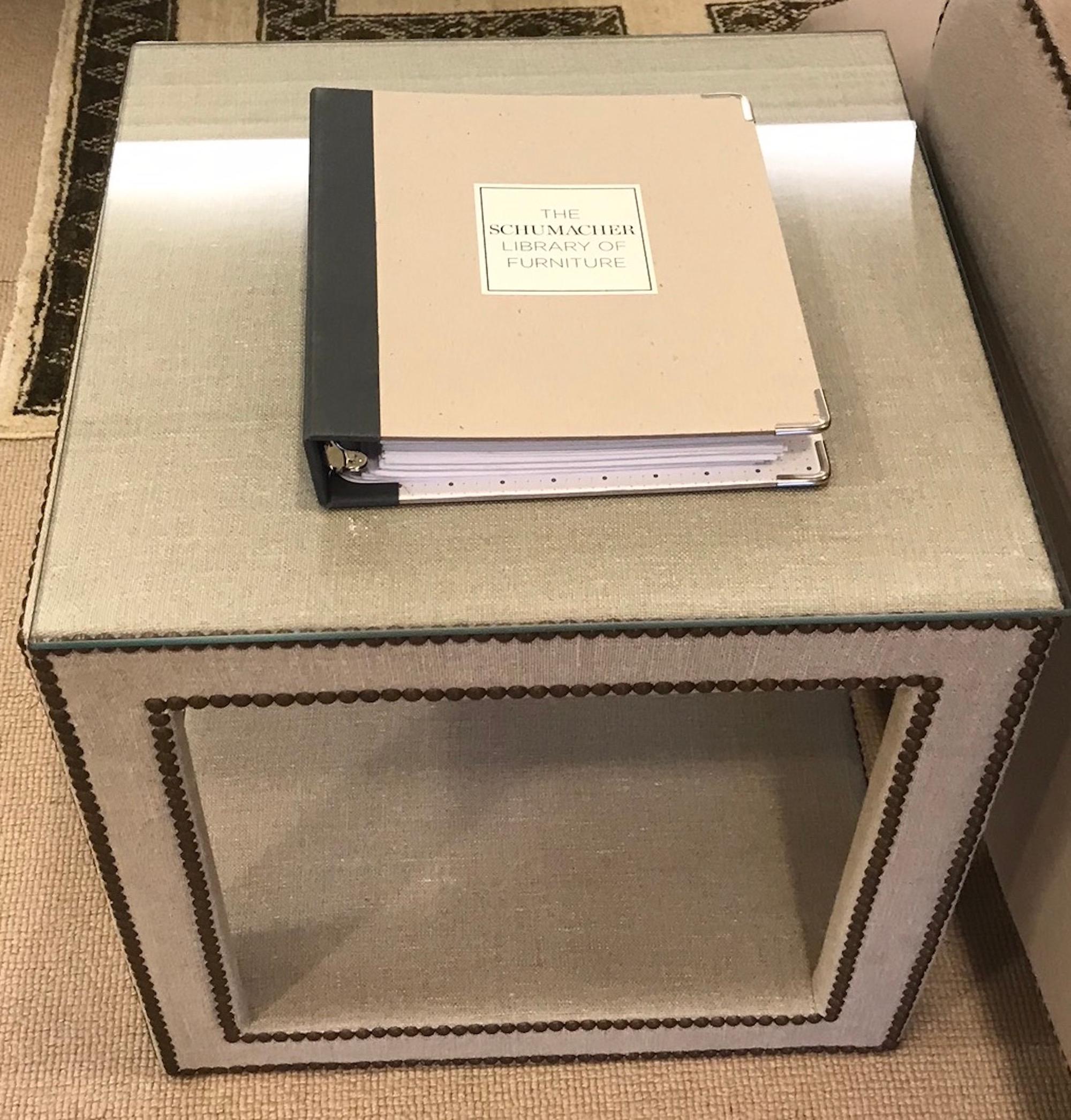 The Baldwin Cube is composed of a hardwood frame that is fully upholstered in Gweneth Linen Schumacher fabric in linen and is finished with nailhead detailing around the edges and side of the piece. It functions as a chic side table or accessory