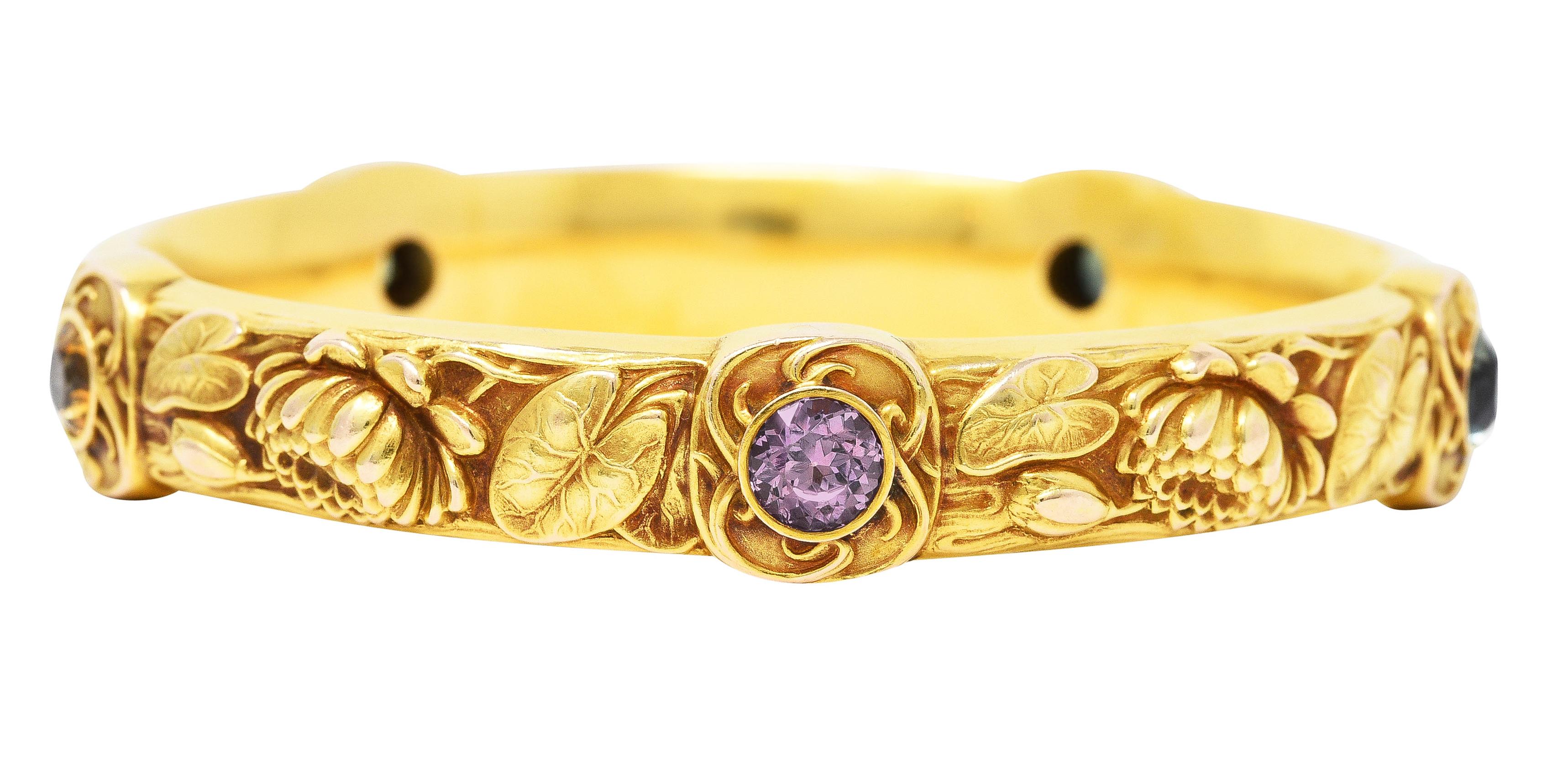 Designed as a gold bangle with repoussé lily pads and lotus flowers winding throughout. Featuring five cushion shaped stations each centering bezel set round cut Montana sapphires approximately 5.50 carats total. Light lavender, light green, light