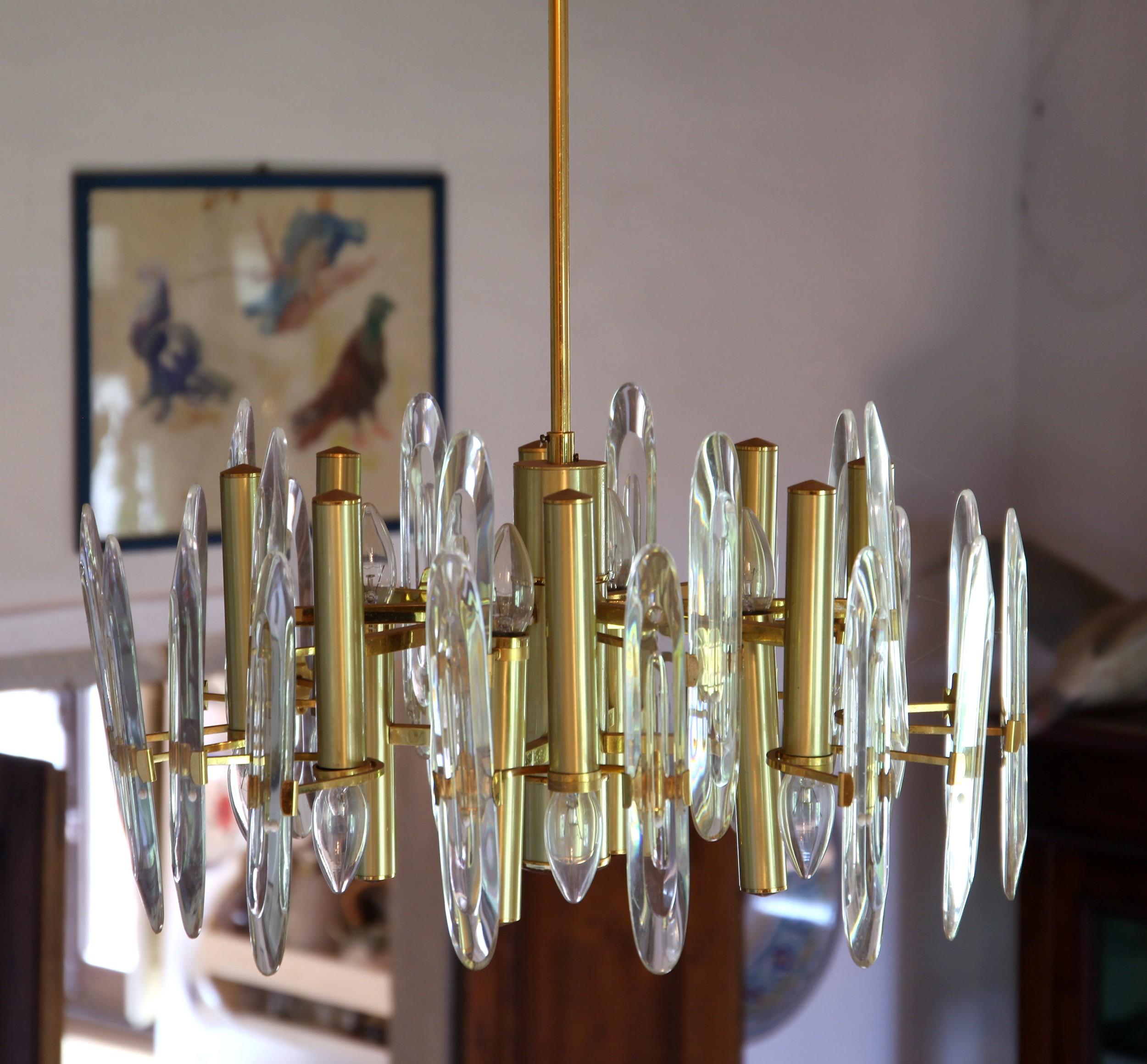 Lampadario a dodici luci di Gaetano Sciolari, produzione realizzata per Stilkronen, Italia, anni Settanta.
Otto luci in basso e quattro luci in alto. Ottone placcato oro. Elementi trasparenti in cristallo Led.
Le lampadine sono circondate da 24