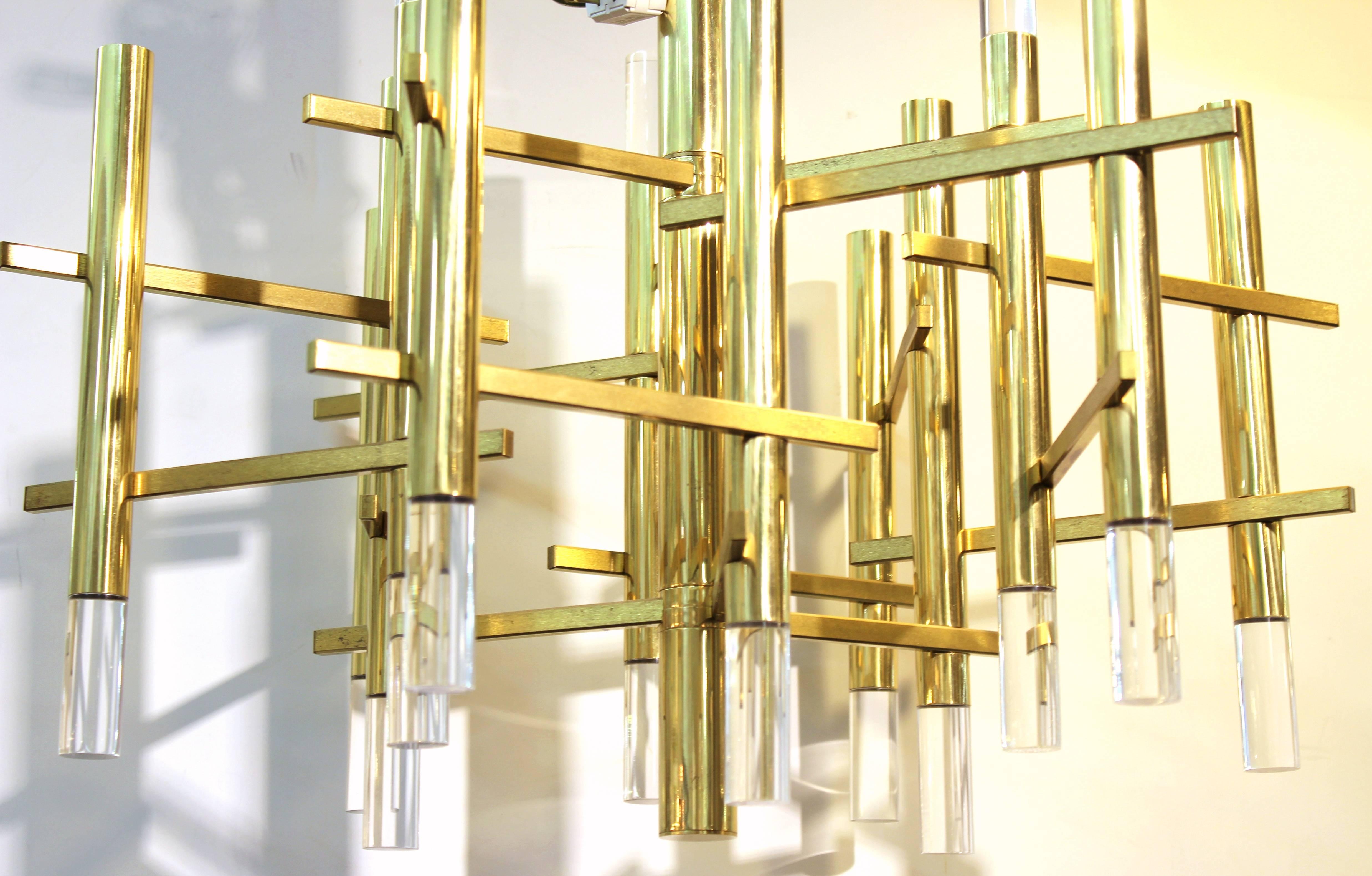 An atomic era chandelier by Sciolari with cylindrical brass arms, each capped with Lucite prisms either on the top or bottom. The cylindrical arms are connected by horizontal brass arms and create a star-like shape when viewed from beneath. The