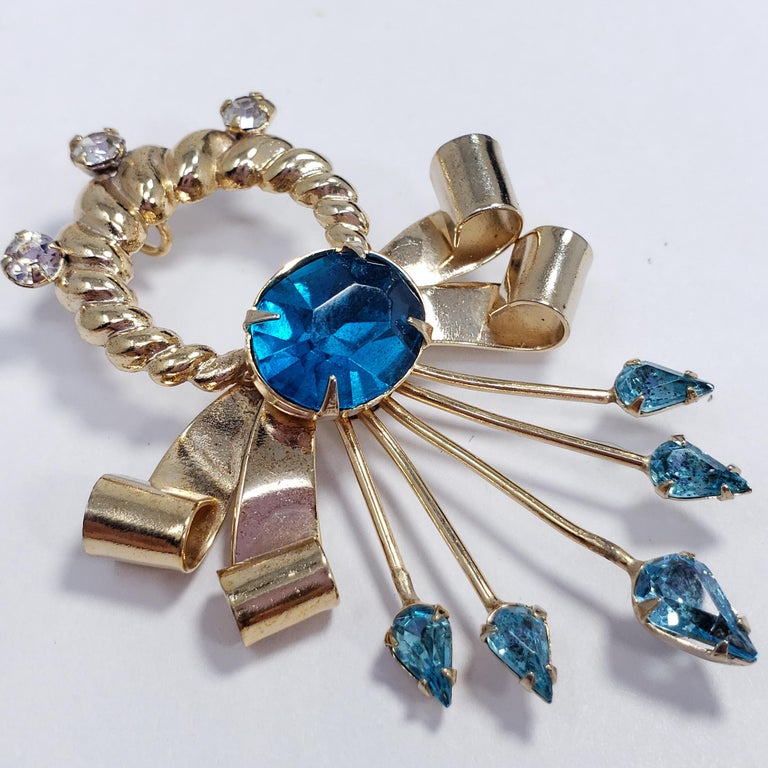 A luxurious accessory by 1950s fashion jewelry designer Scitarelli. This pin brooch can also be worn as a pendant and features stylish goldtone bow motifs accented with cyan-blue crystals. 

Hallmarks: Scitarelli
