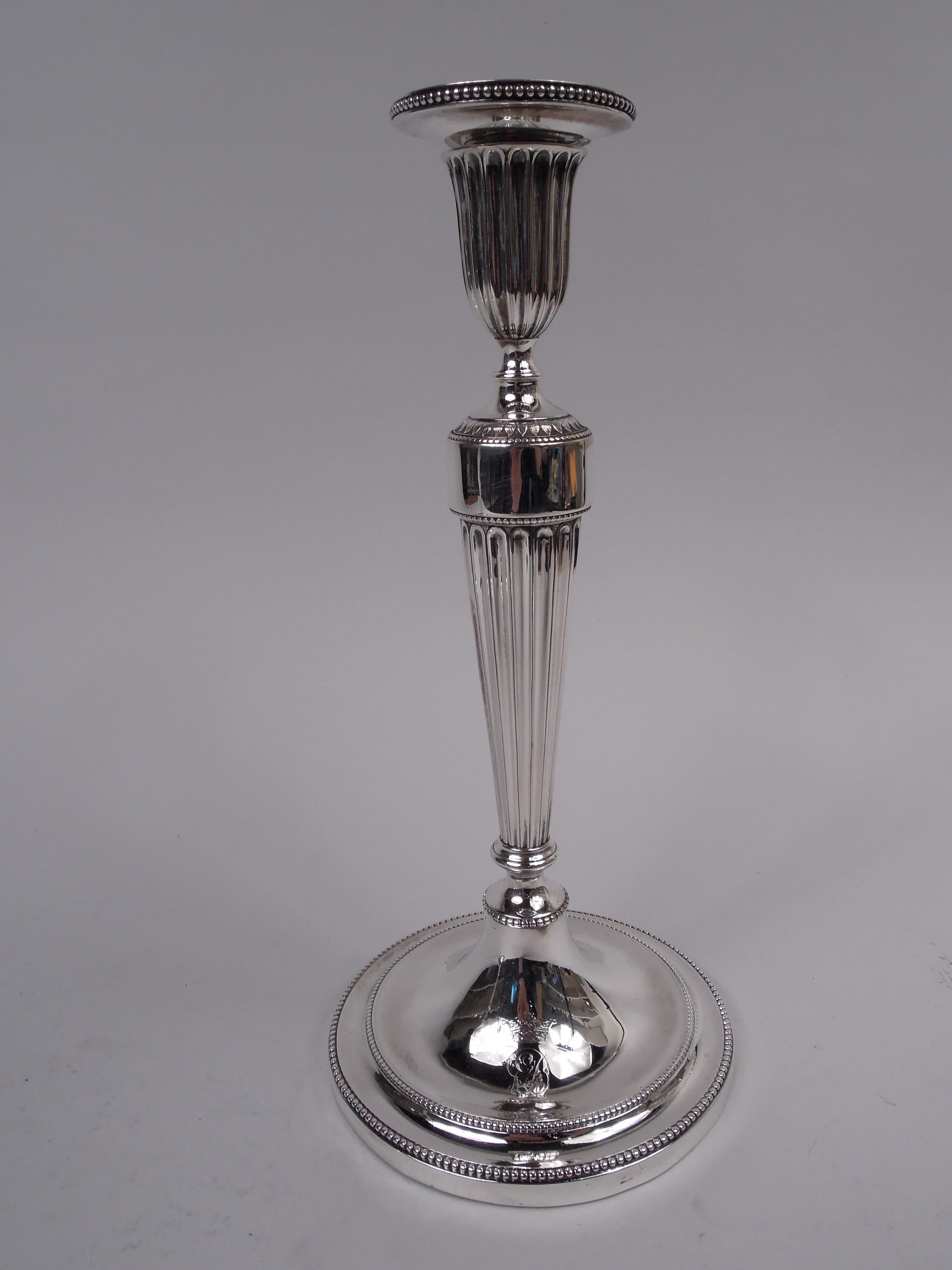 Pair of George III sterling silver candlesticks. Made by John Scofield in London in 1790. Each: Tapering socket with detachable bobeche mounted to tapering and knopped columnar shaft with raised leaf-and-dart ornament on shoulder; raised foot.
