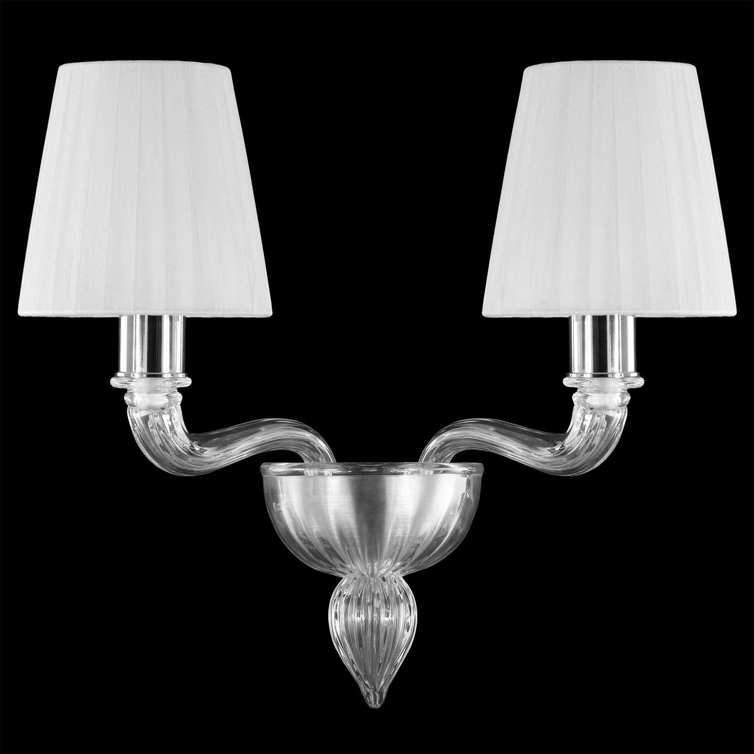 Coco sconce with 2 arms in clear Murano glass with white colour organza handmade lampshades by Multiforme.
The Murano glass Coco collection takes inspiration from Coco Chanel, the revolutionary woman that has changed the fashion industry during the