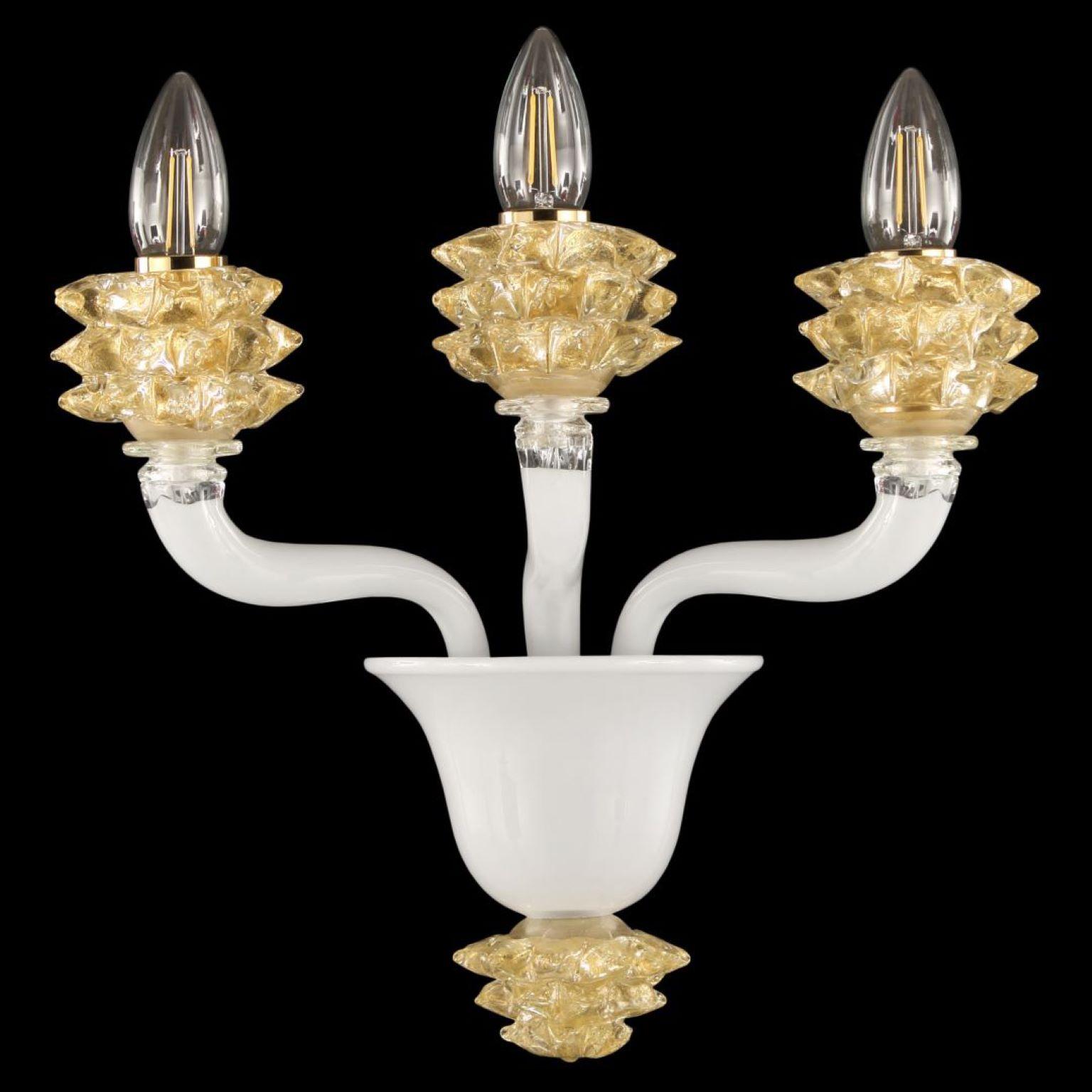 The Diamante sconce with 3 arms in white encased Murano glass and gold details is a well proportioned product.
The glass of the arms is smooth. The standout elements of this sconce are the cups, which are created using a complex manufacturing