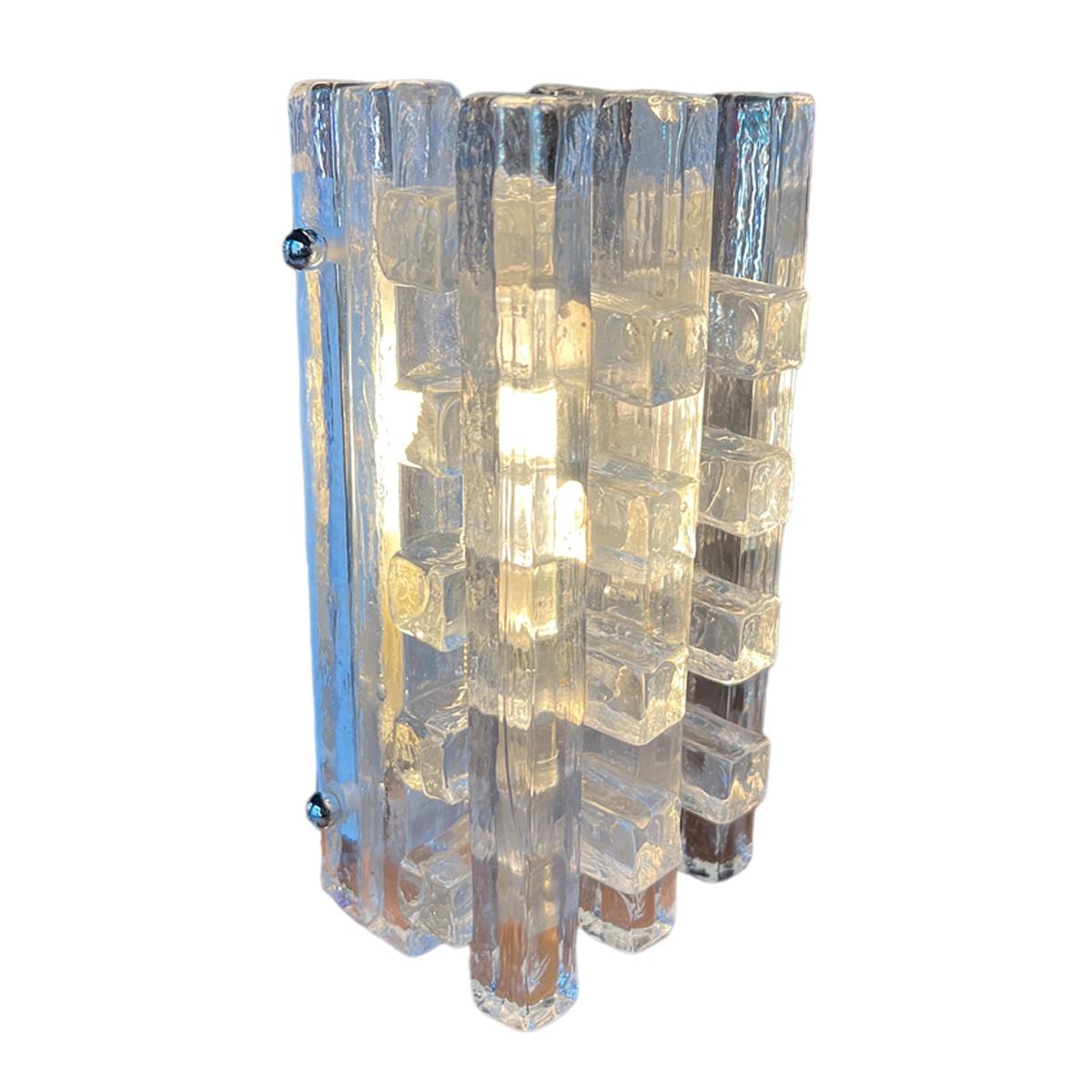 Mid-Century Brutalist Wall Sconce by Albano Poli for Poliarte, 1970
This wall sconce embodies the essence of the 1960s-1070s. It features approximately twenty stacked Murano glass rectangles of various sizes, all transparent yet textured, creating a