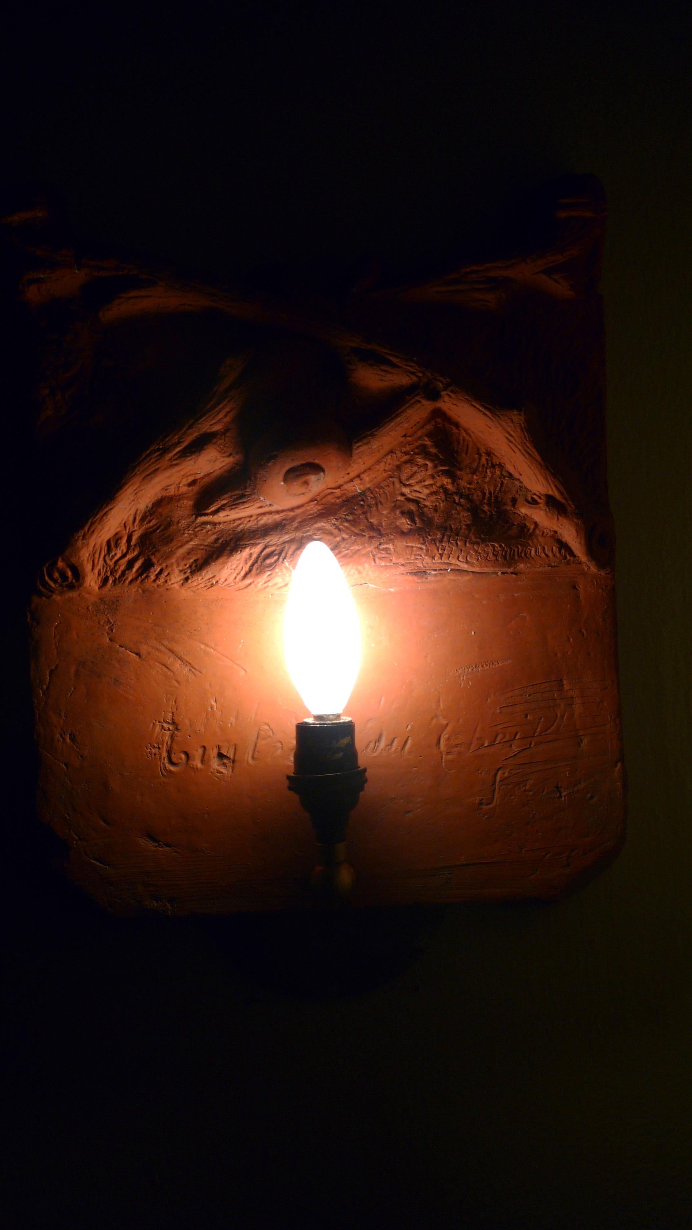 Early 1700s French terracotta garden stone signed by the artist. Has been made into a hallway sconce. Mysterious, earthen, tactile. Depicts snail crawling amongst ground cover. Professionally wired candelabra socket and bulb is hardwired into