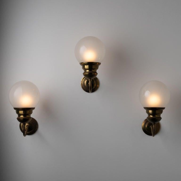 Applique di Luigi Caccia Dominioni per Azucena. Progettato e prodotto in Italia, intorno agli anni '1960. Classica lampada a braccio ricurvo composta da un globo di vetro acidato, posto in cima a un braccio di ottone ricurvo. Ogni applique contiene