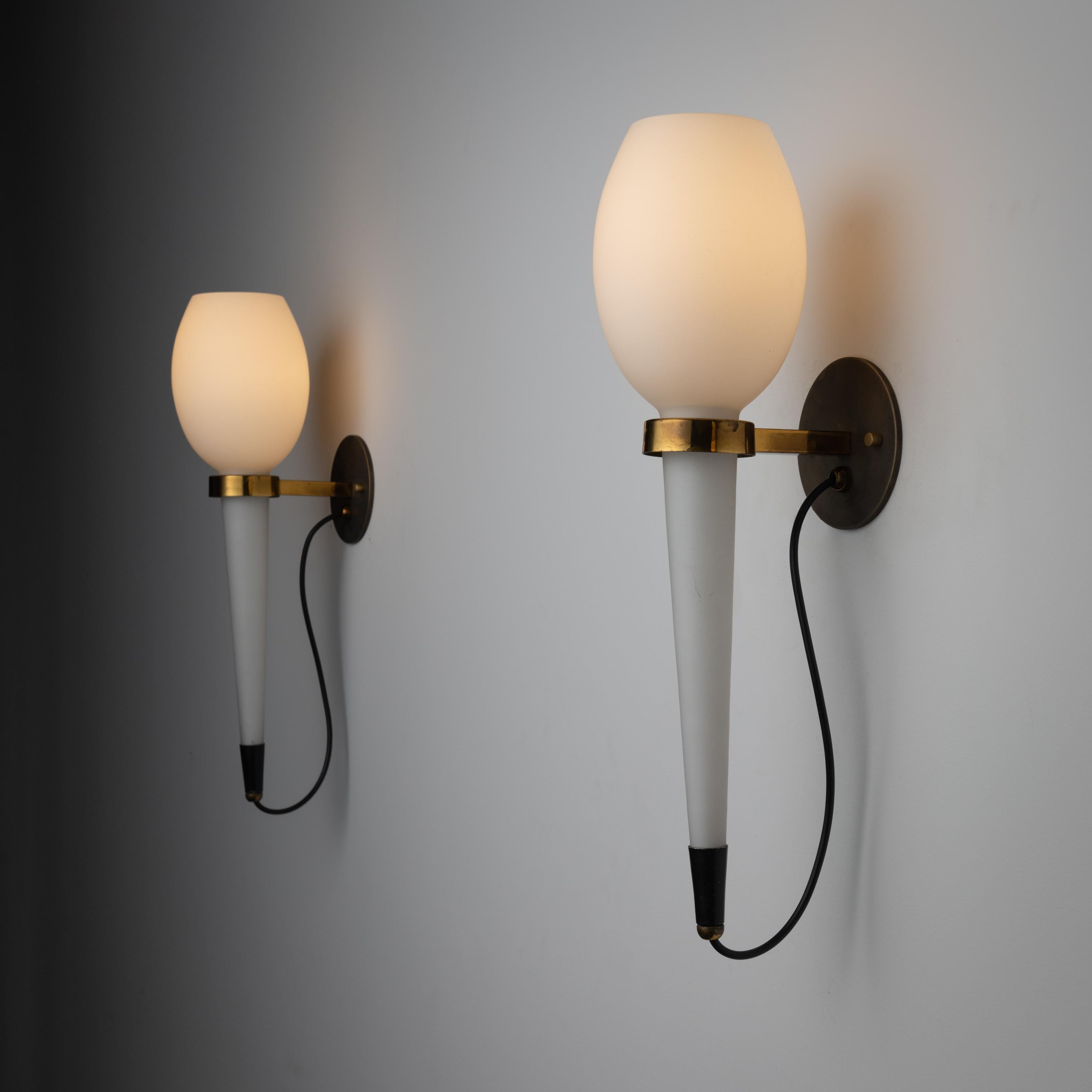 Sconces by Stilnovo. Designed and manufactured in Italy, circa 1960. Beautiful milk glass tulip sconces with a polished brass clasp that adheres to the backplate. Each sconce holds one E27 bulb, adapted for the US. We recommend using 40w maximum E27