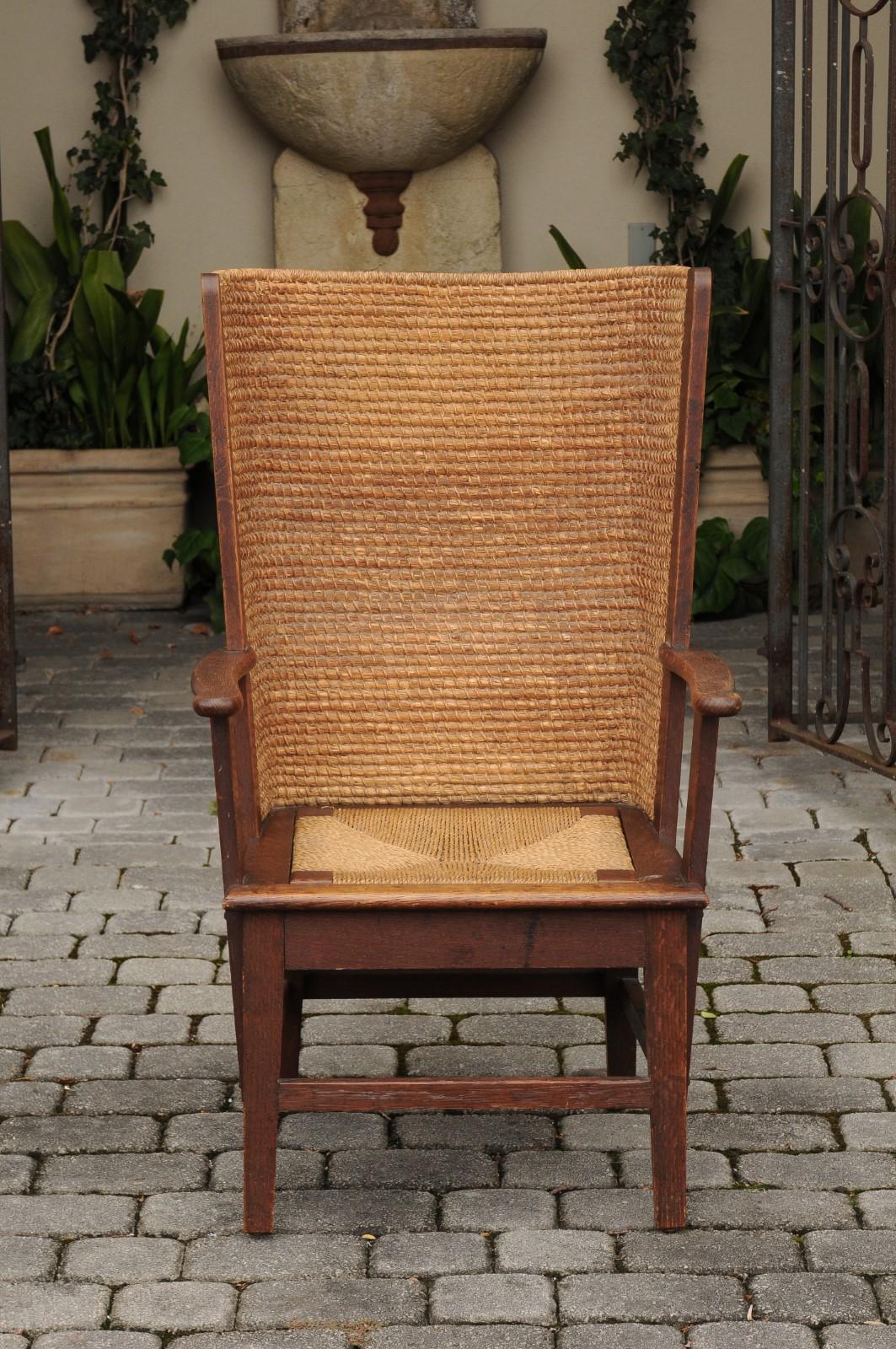 A Scottish Orkney Island oak wingback chair from the early 20th century with handwoven straw back, rush seat, open arms, straight legs and side stretchers. Born at the Turn of the Century in the archipelago of Orkney off of the northern coast of