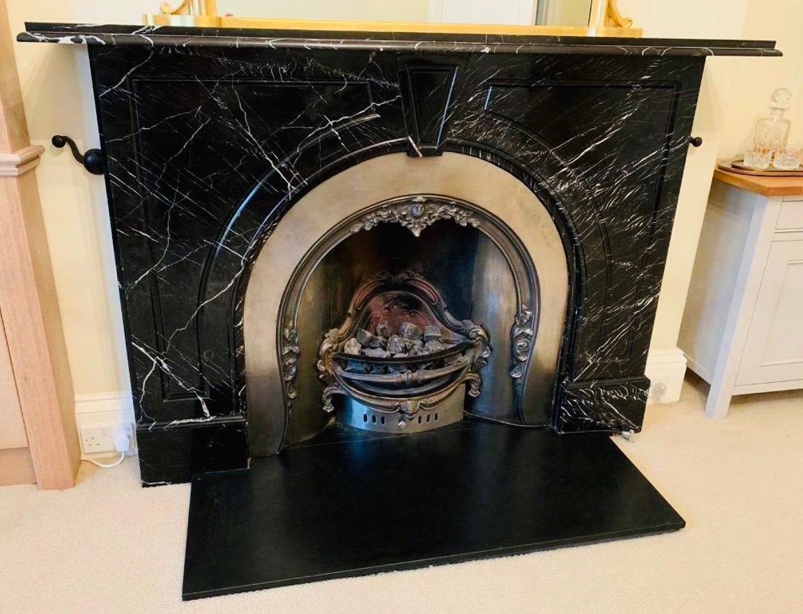 A large Scottish 19th century late Victorian arched fireplace surround carved in black marble with subtle white veining. A generous top shelf with a double moulded edge, sits above a central keystone flanked by tall fielded panel spandrels resting
