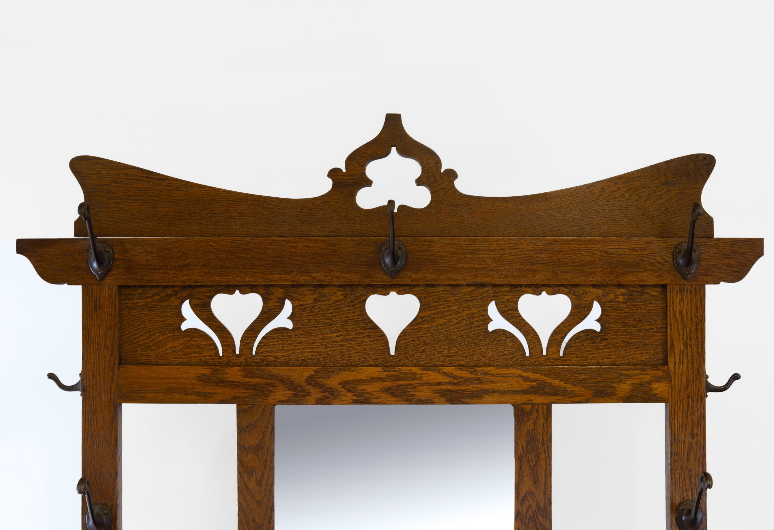 Scottish Arts & Crafts oak hallstand. Circa 1890. Copper maker's label: A Gardner & Sons, Glasgow.

Made in solid oak, with stylised heart and trefoil cut out decorations. The stand has a bevelled central mirror with a glove box below, and a