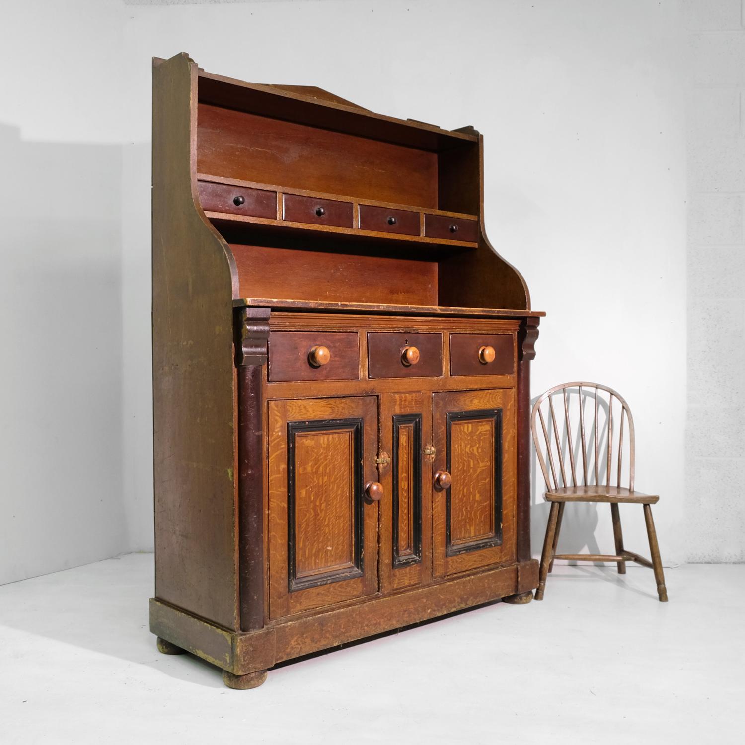 A substantial antique Scottish dresser in pine with its original scumbled finish and ebonised and plum-painted details. The upper structure with simple, unfussy shape has two shelves and a run of four small drawers. This is above the main work