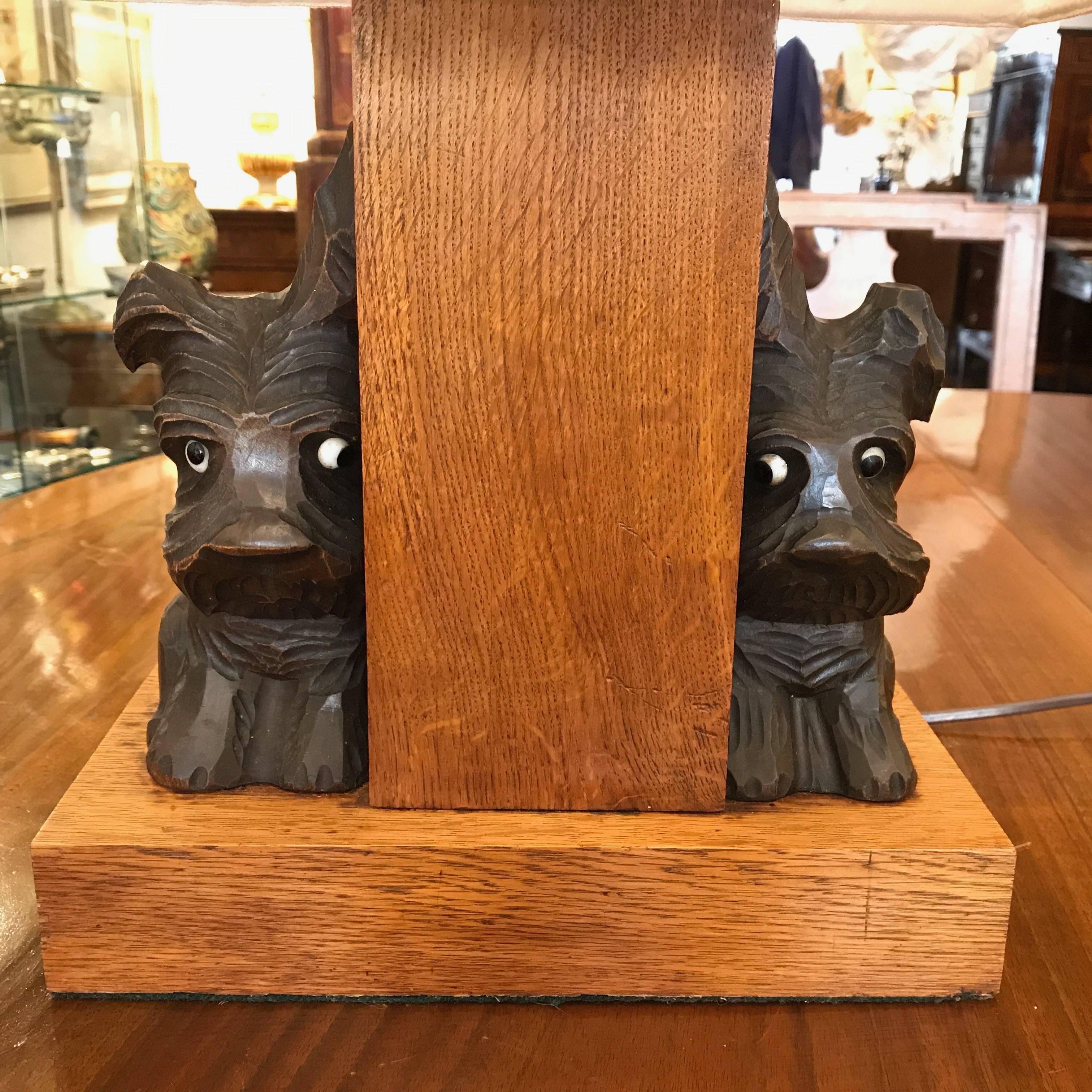 A funny oak table lamp, of French origin, with solid oak  rectangular base decorated with two hand carved and ebonized seated Scottie dogs with glass eyes. 
Hand made white fabric lamp shade.  
One Edison 27 light bulb.
It is in excellent condition,