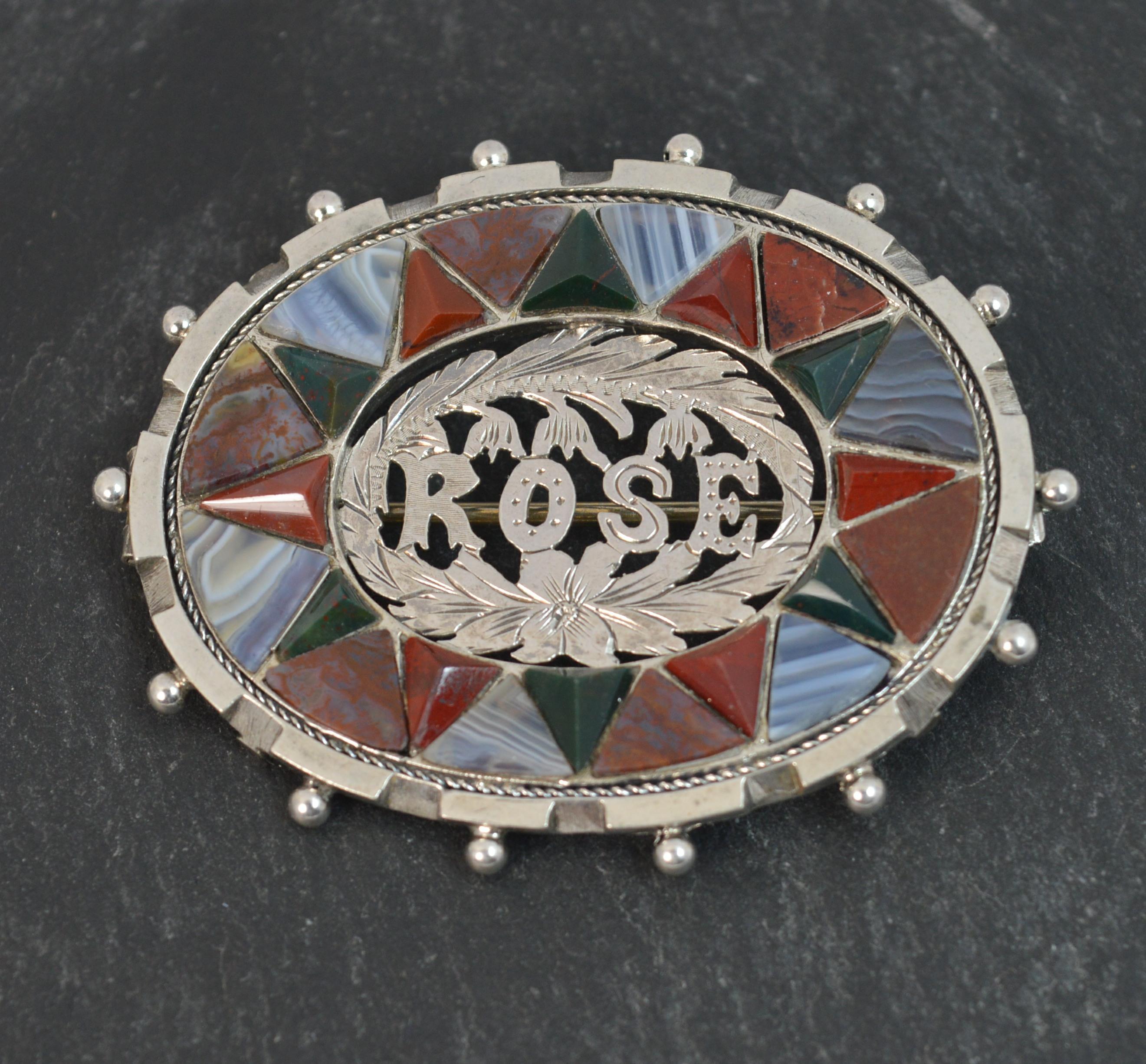 A beautiful quality late Victorian period brooch. Oval shaped example in sterling silver.
Designed with a silver ball border. Pierced ROSE silver section to centre. The border with flat triangular shaped agates of two varieties and colours and