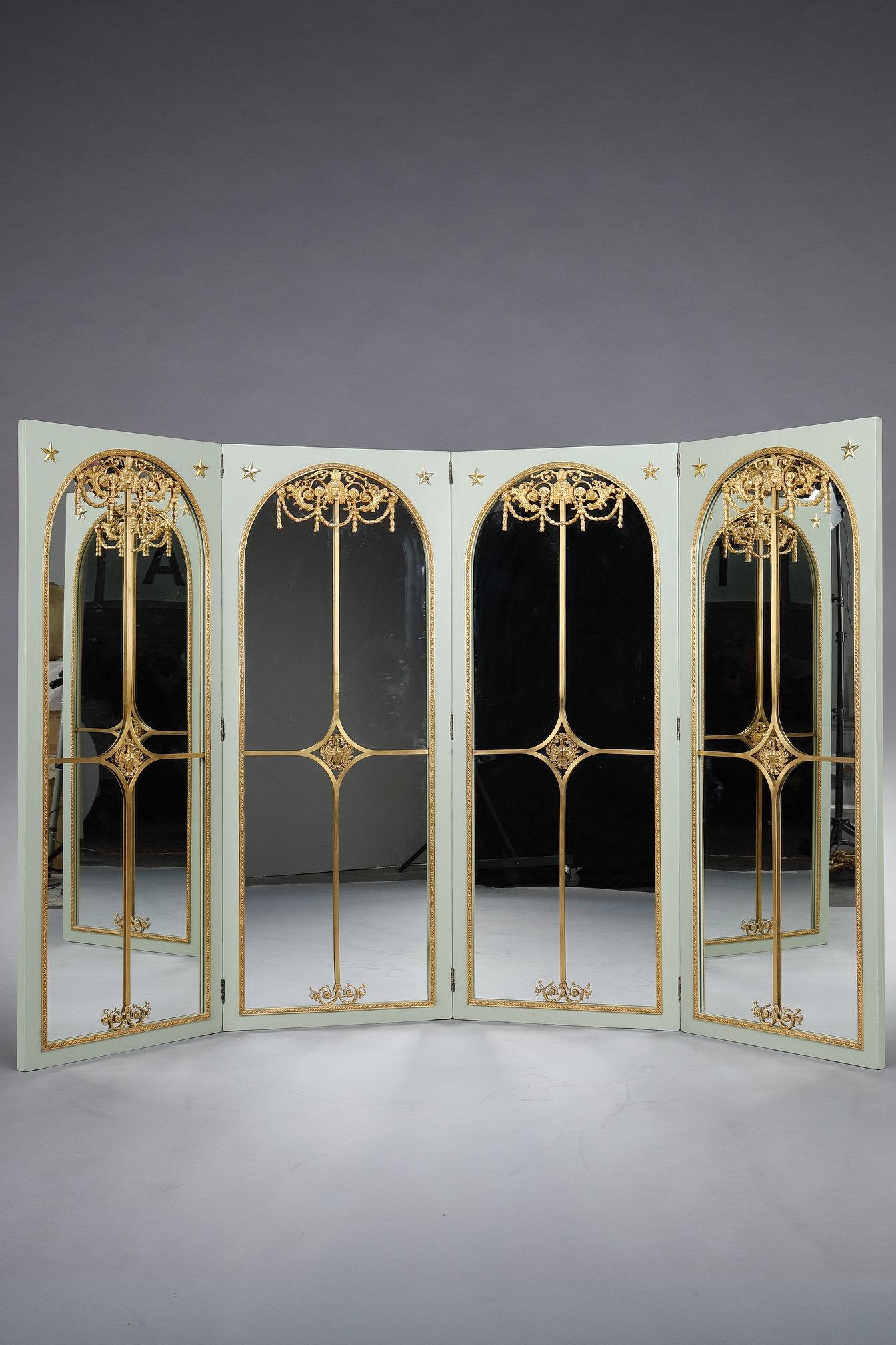 Four-leaf screen in an empire green lacquered wood frame. The main face is richly decorated in gilded bronze with Commedia dell'Arte masks, foliage, garlands, stars, a cross and a swan in the center. This decoration is superimposed on mirrors, the