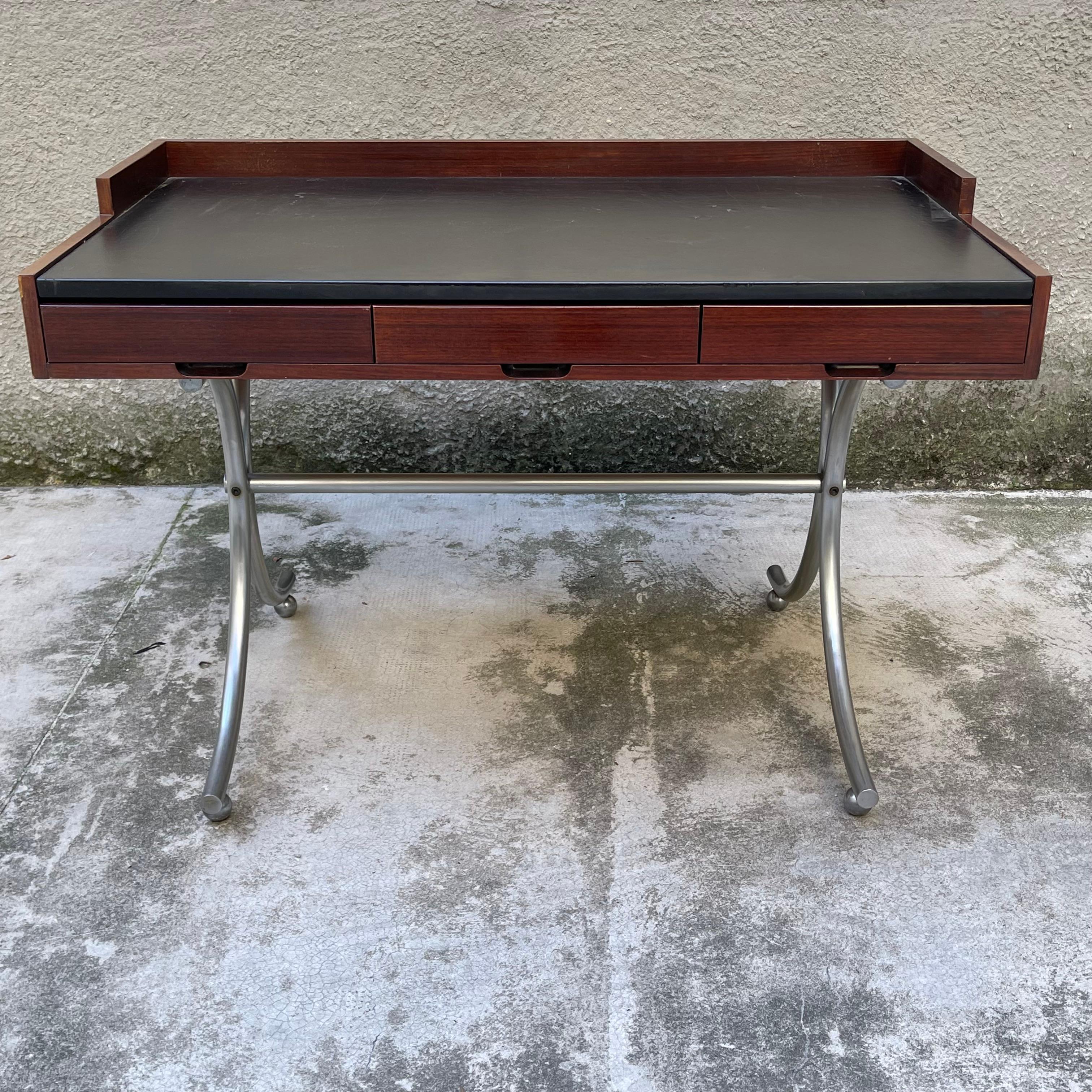 Piccola scrivania con tre cassetti, struttura in legno e supporti in tubolare metallico cromato e curvato. 
Lo scrittoio presenta un lieve difetto su un fianco, come mostrato in foto.
Prodotto da Arlex, Italia, dal 1962. Bibliografia (modello