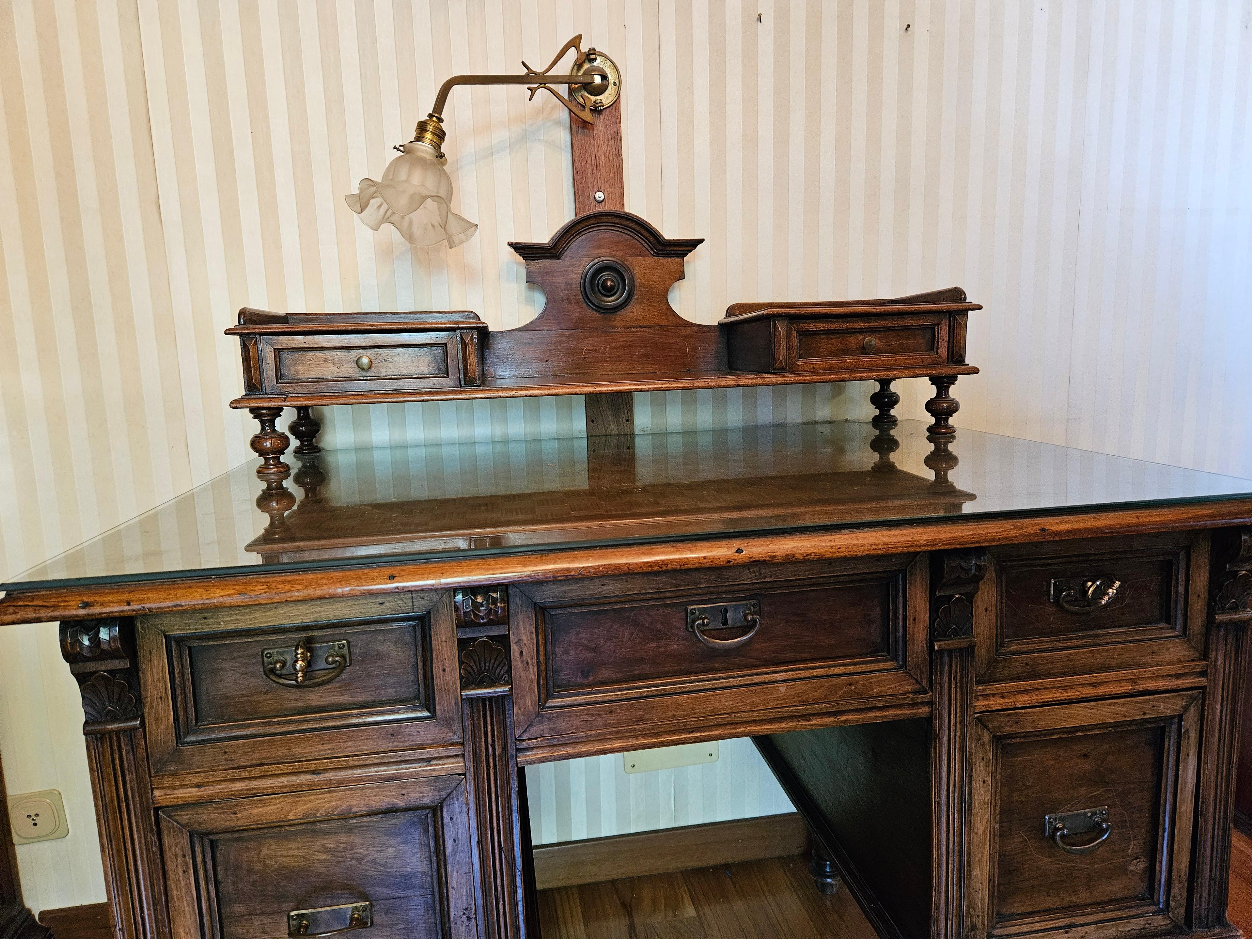 Venetian walnut writing desk with an ornate glass-protected top and a set of large, sturdy drawers.

On the main top we find two side drawers with a two-way glass light, down a pair of drawers on the right and left plus a central one.

Various