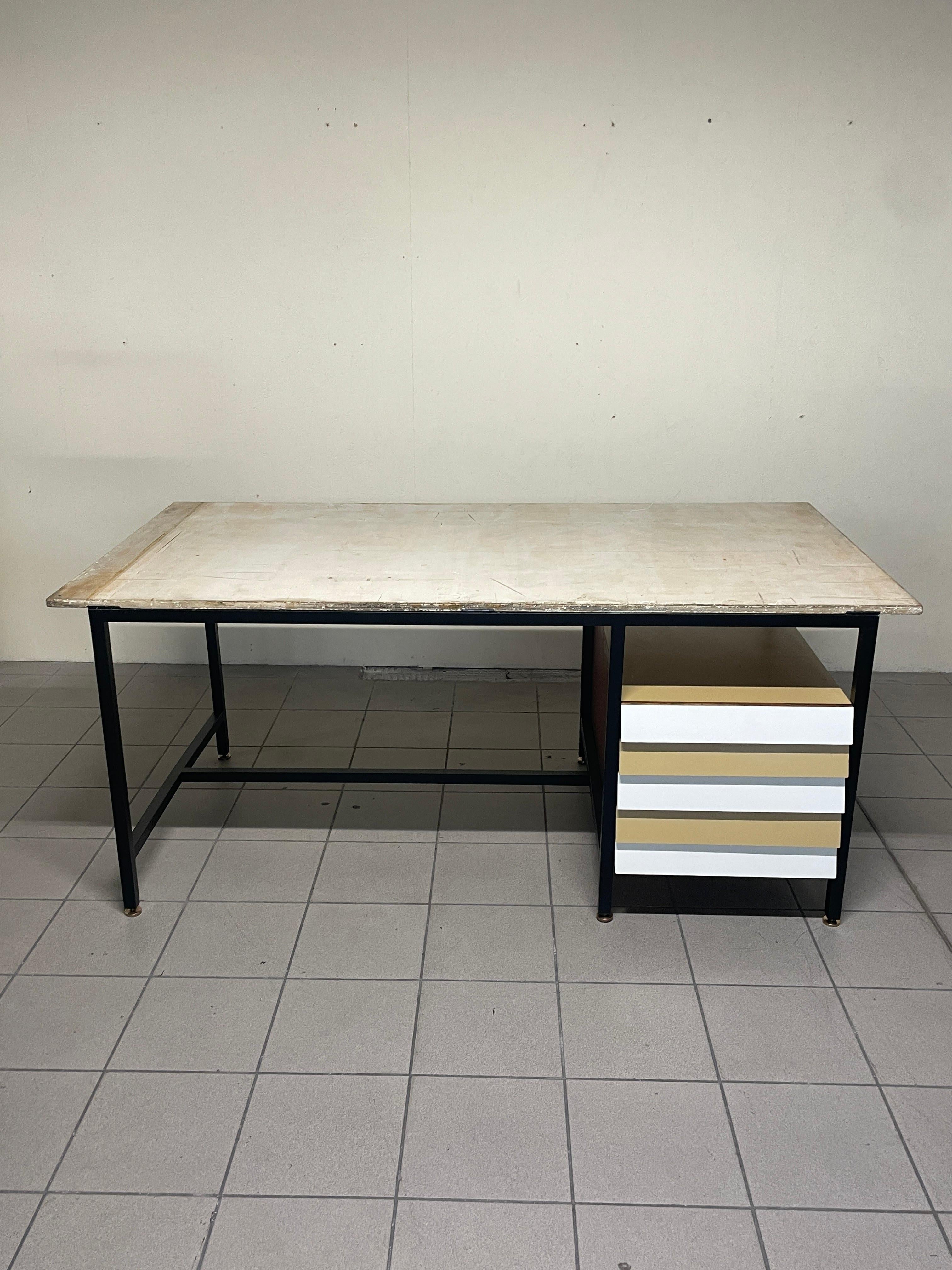Bureau à plateau basculant datant des années 1960, appartenant à un cabinet d'architectes.

Cadre en fer tubulaire laqué noir avec pieds en laiton réglables en hauteur.

Commode en bois avec façades en stratifié coloré.

Le plateau basculant en
