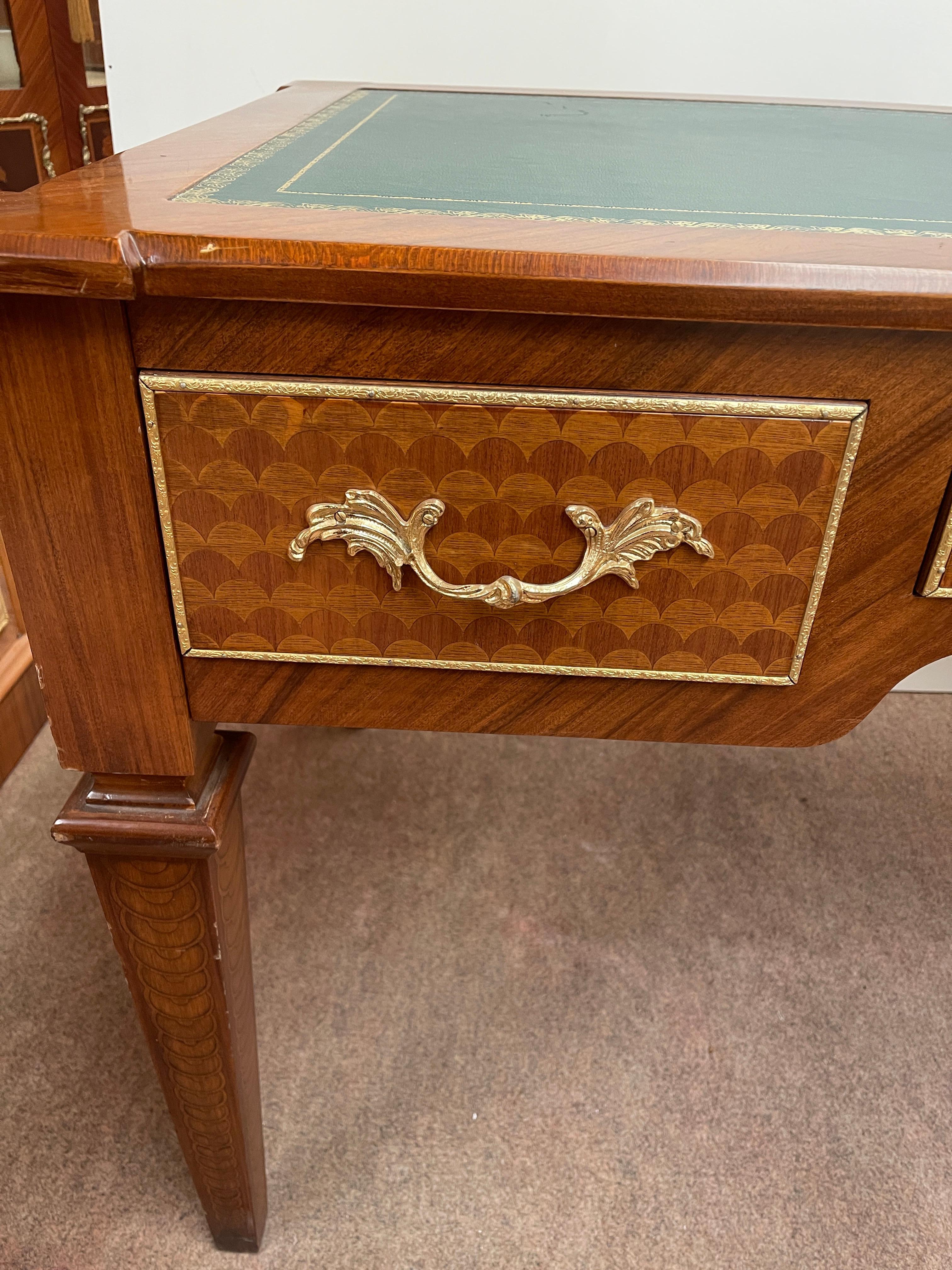 Magnificent classically inspired study desk, an elegant and functional piece of furniture that combines the beauty of fine woods with the refinement of leather and bronzes. The top is upholstered in dark green leather, edged with a golden decorative