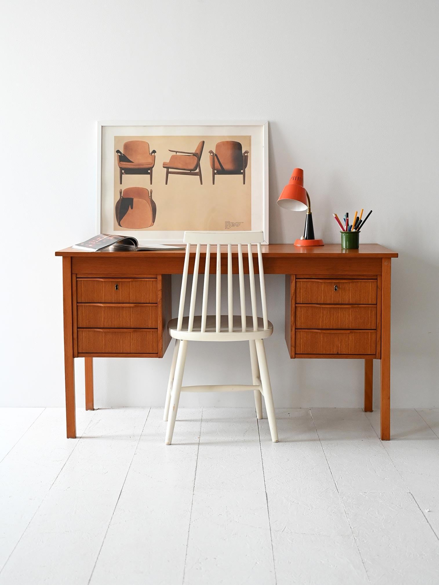 Scrivania con doppio blocco cassetti, maniglie scolpite e gambe squadrate, in teak con finitura calda e uniforme.

Linee nette e simmetria funzionale per questa scrivania scandinava anni ’60 in teak. I due blocchi laterali ospitano tre cassetti