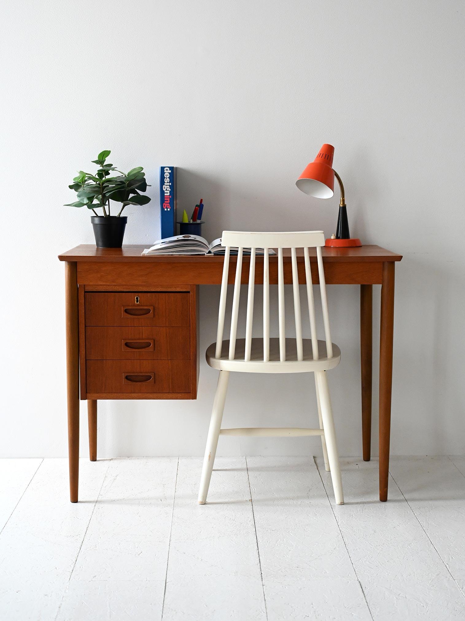 Scrivania con tre cassetti laterali, maniglie intagliate squadrate e struttura leggera in teak. Chiave non disponibile.

Forma compatta e proporzioni funzionali per questa scrivania scandinava vintage in teak. I tre cassetti sul lato sinistro
