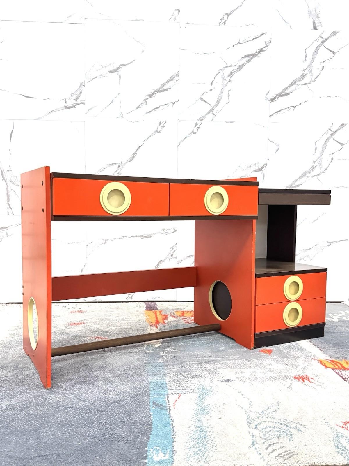 Ikonischer Schreibtisch aus den 1970er Jahren im Space-Age-Stil, aus Holz mit lackiertem Rahmen in Orange- und Brauntönen und beigen Kunststoffdetails. Das kühne, geometrische Design ist typisch für die futuristische Ästhetik der damaligen Zeit, mit