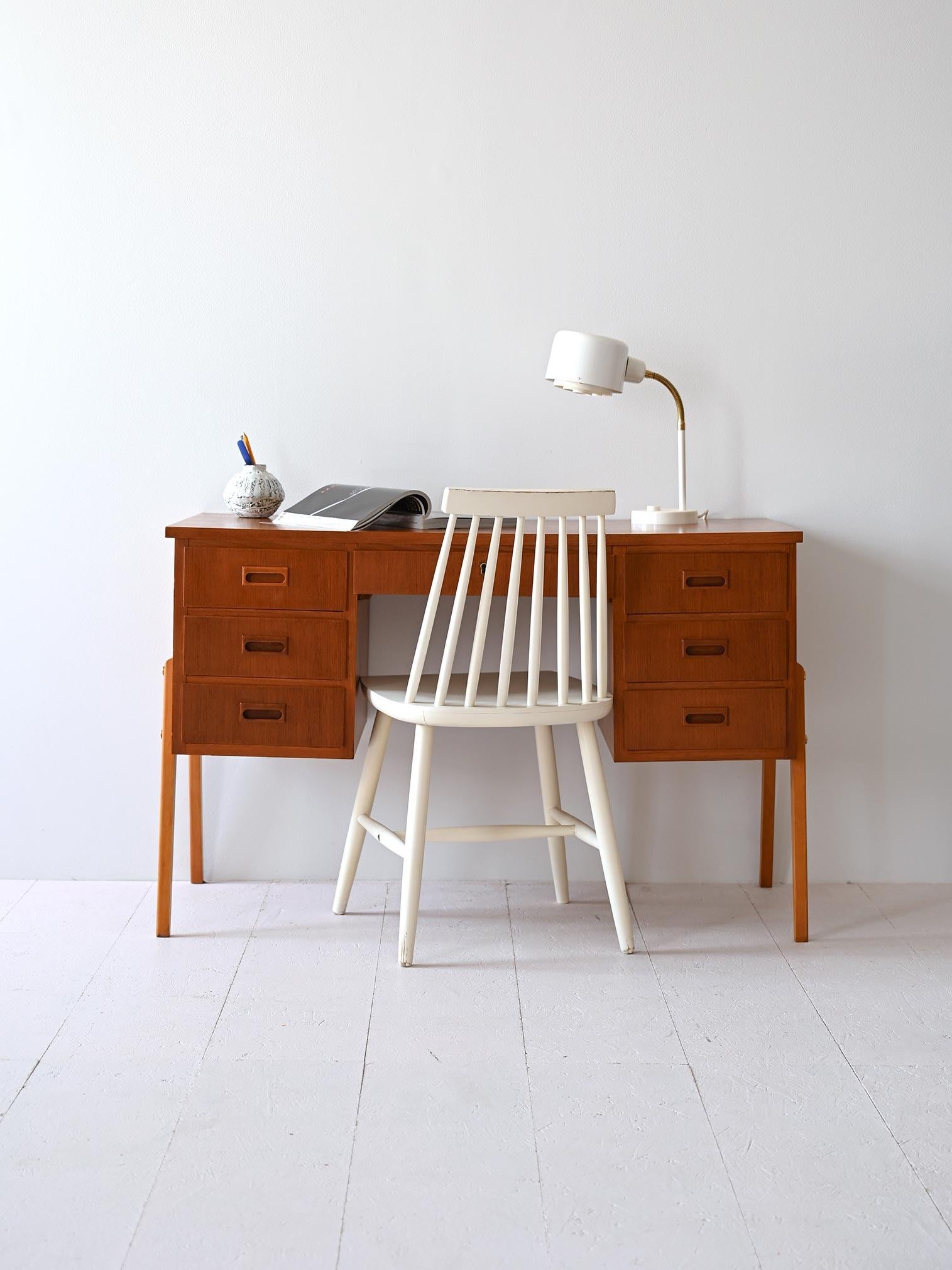 Un pezzo d'arredo originale degli anni '60 in teak. Ai lati vi sono rispettivamente 3 cassetti con l’impugnatura scolpita nel legno, mentre al centro vi è un cassetto con serratura. 

Le gambe, realizzate in legno chiaro, contrastano piacevolmente