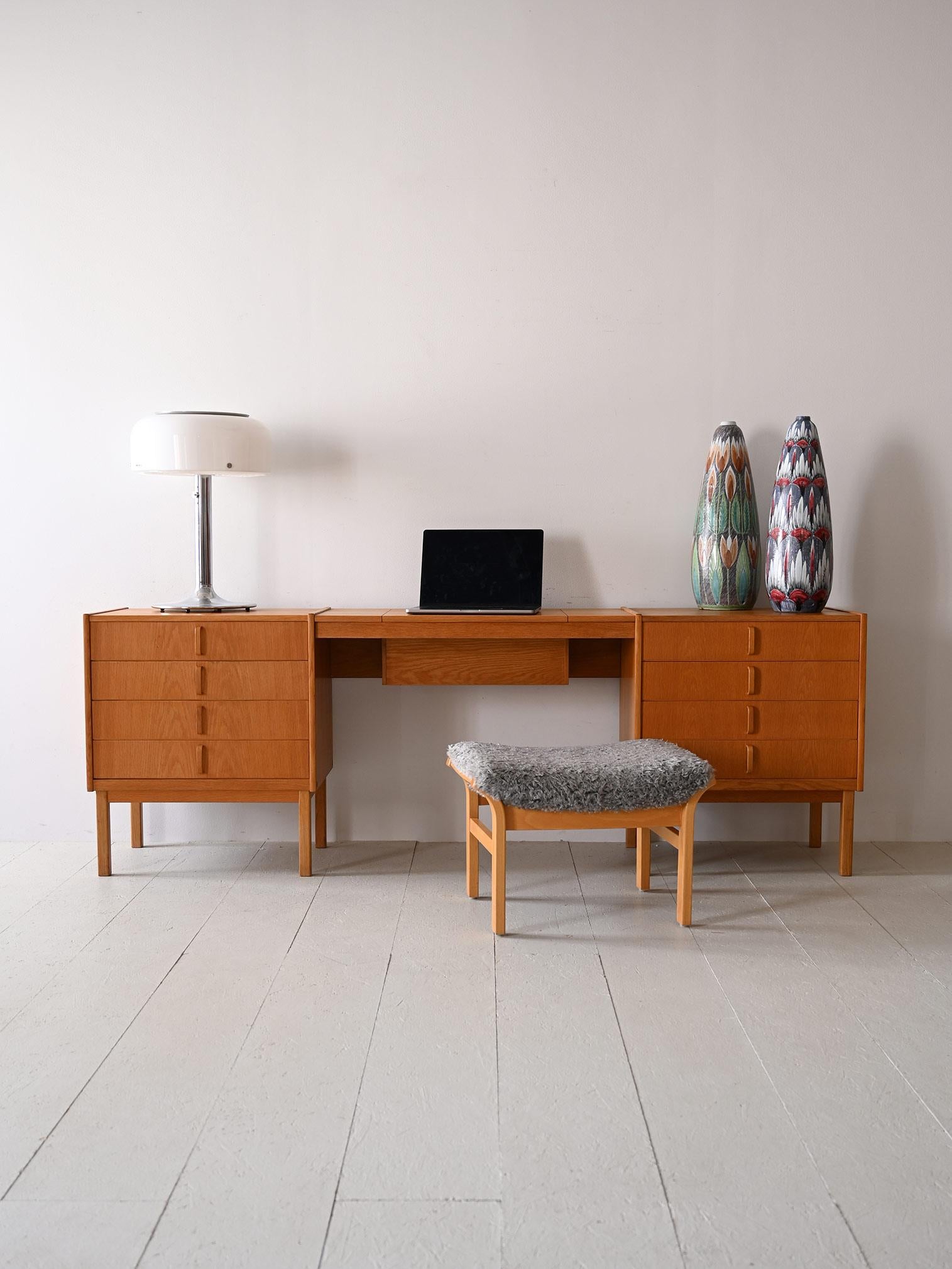 This 1960s Scandinavian desk made of oak wood consists of two drawers and a central desk. 
The distinguishing feature is a hidden mirror that, when raised, transforms the cabinet into a dressing table, offering dual functionality. 
The two side