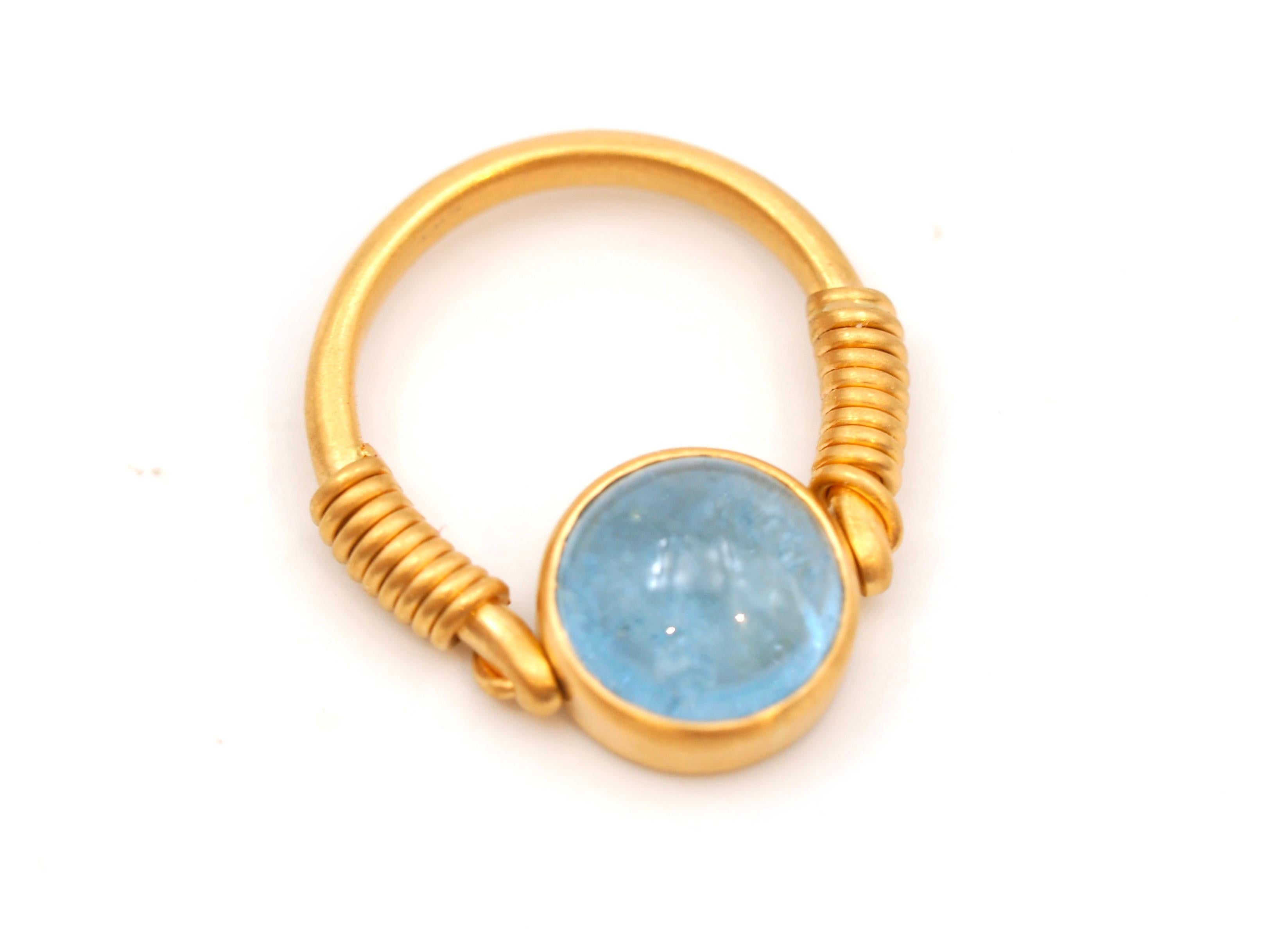 This antic style ring by Scrives is set with an aquamarine cabochon of 3.74cts. The stone is natural with no treatment. It shows visible natural inclusions.  
The stone is set in a 22kt gold settle and can turn arrowed the gold wire so it gives more