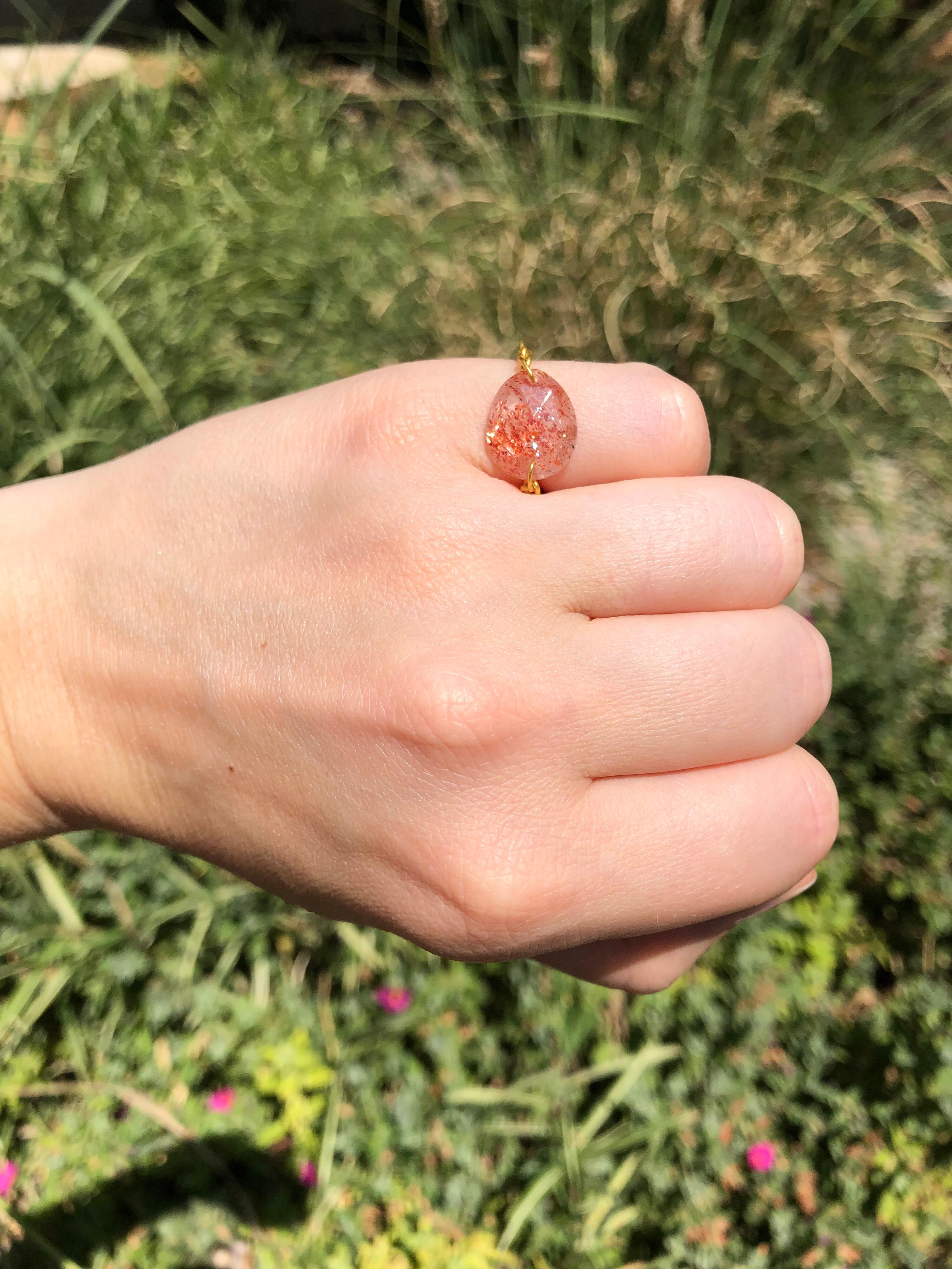 Dieser Ring von Scrives besteht aus einem facettierten Sonnenstein von 4,83 Karat, der einfach auf jeder Seite gebohrt wurde, um eine handgefertigte 22 Karat Goldkette hinzuzufügen. 
Der Sonnenstein ist naturbelassen und zeigt die typischen