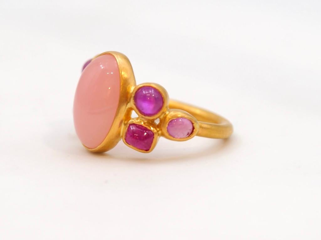 Dieser zarte Ring besteht aus einem Pfirsich-Chalcedon-Cabochon von 5,25 ct, umgeben von 6 rosafarbenen Saphir-Cabochons (Gesamtgewicht: 3,06cts). Die Steine sind naturbelassen mit typischen Einschlüssen. 
Der Chalzedon hat eine ovale Form. Er hat
