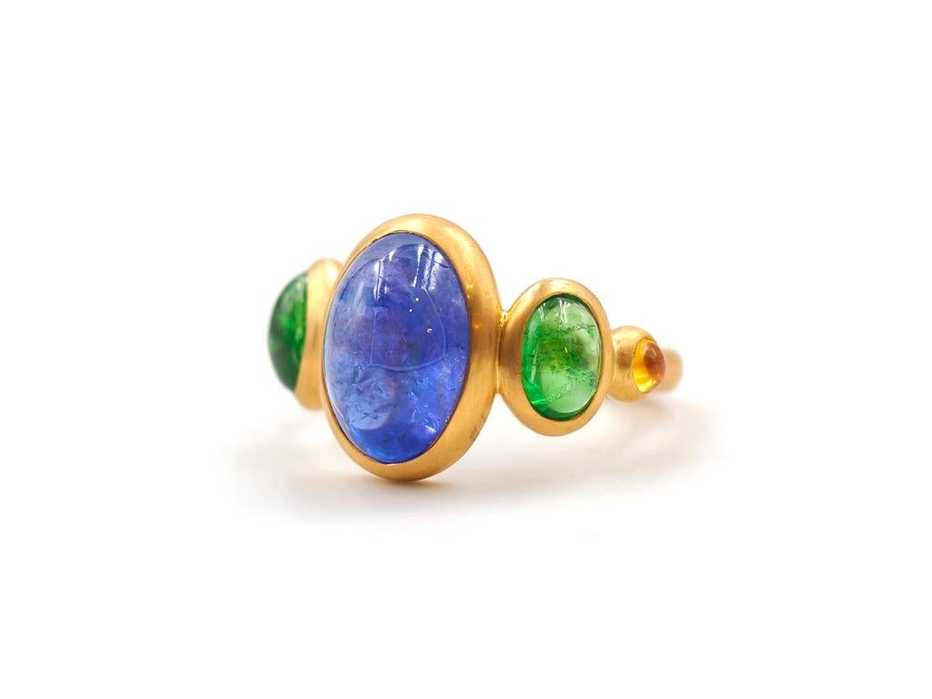 This delicate ring is composed of 5 stones in line: 1 Tanzanite cabochon, 2 Tzavorite (green garnet) cabochons and 2 natural orange sapphire cabochons. The center stone is a tanzanite of 5.85 cts and the 2 tzavorites have a total weight of 2.12 cts.