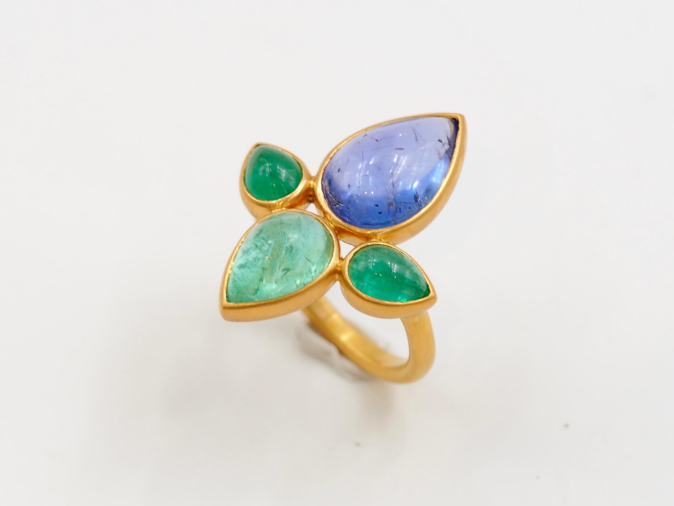 This one-of-a-kind ring is composed of 3 natural emerald cabochons (total weight of 5 cts) and a tanzanite cabochon of 5.9 cts. The four stones are organized to form a lotus flower. 

The tanzanite colour is purplish blue. The 2 emeralds of the