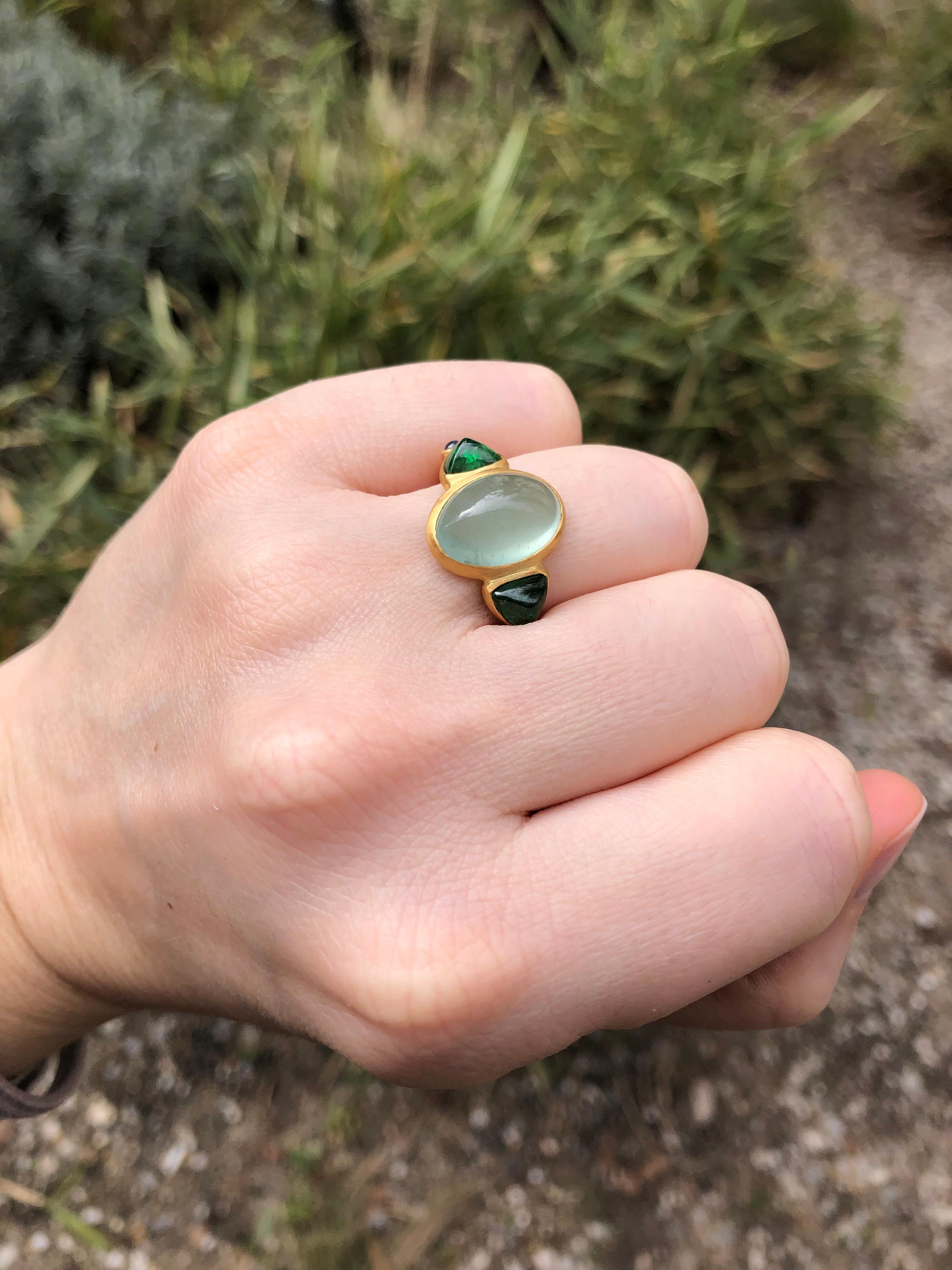 This delicate ring is composed of 5 stones in line: 1 green Aquamarine cabochon, 2 trillion tsavorite cabochons and 2 blue sapphire cabochons. 
The center stone is an aquamarine of 5.93 cts. The tsavorites total weight is 2.44cts. The 2 sapphire