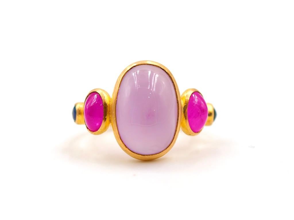 This delicate ring is composed of 5 stones in line: 1 lilac chalcedony sugarloaf, 2 natural ruby cabochons and 2 natural sapphire cabochons. The center stone is a lilac chalcedony of 6.03 cts. It is natural with no treatment. 
The 2 rubies have a