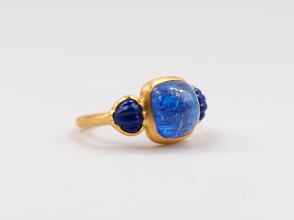This delicate ring is composed of tanzanite cabochon of 6.49 cts surrounded by 2 lapis lazuli carved as shells. The stones show natural, typical and eye-visible inclusions. The inclusions bring a lot of light and live to the stone that contrast with