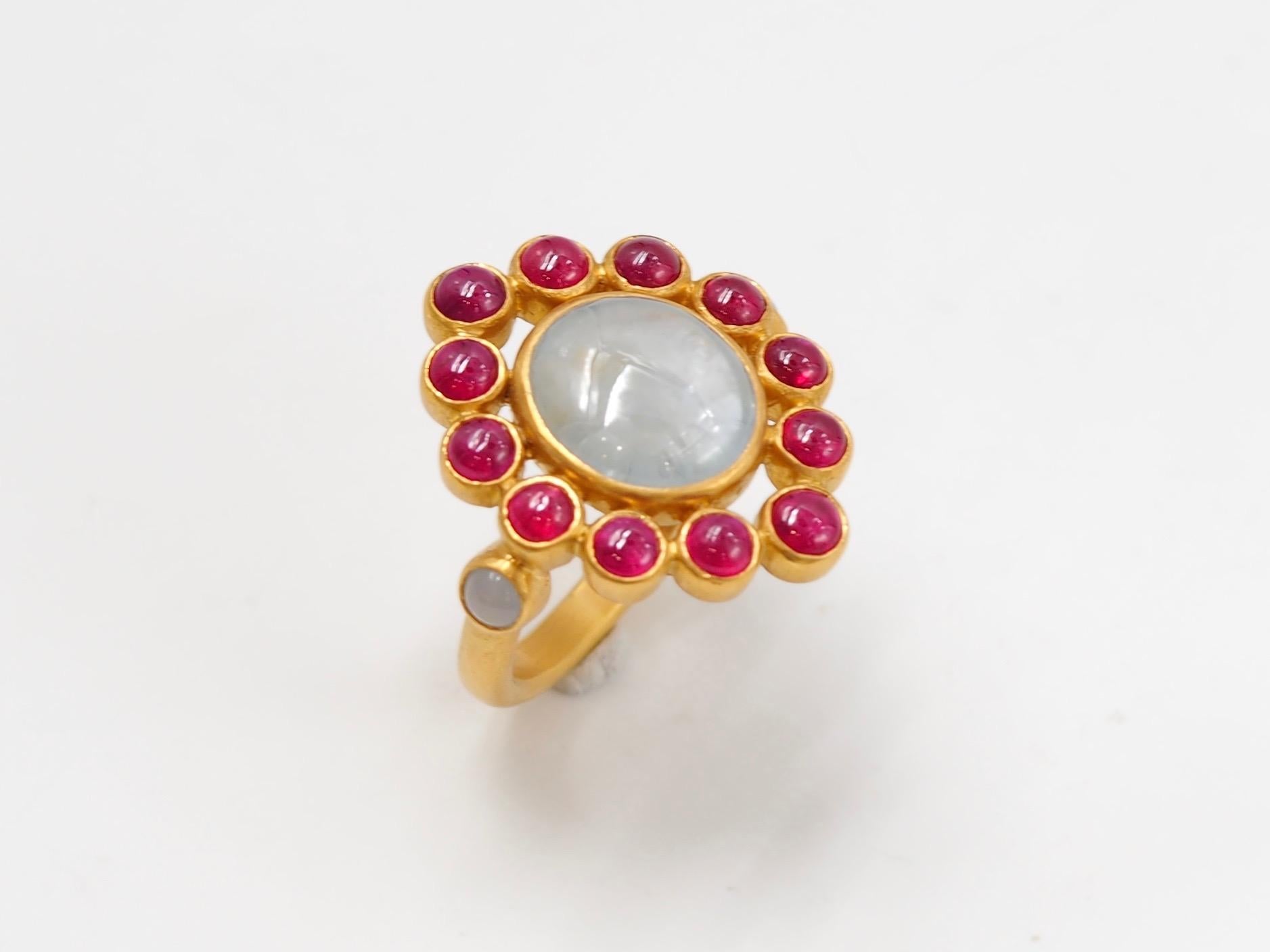 This one-of-a-kind ring by Scrives is composed at its centre of an oval grey sapphire cabochon of 6.7 carats natural & without treatment. The sapphire origin is Burma / Myanmar.
It is surrounded by 12 round Rubies cabochons (total weight of rubies: